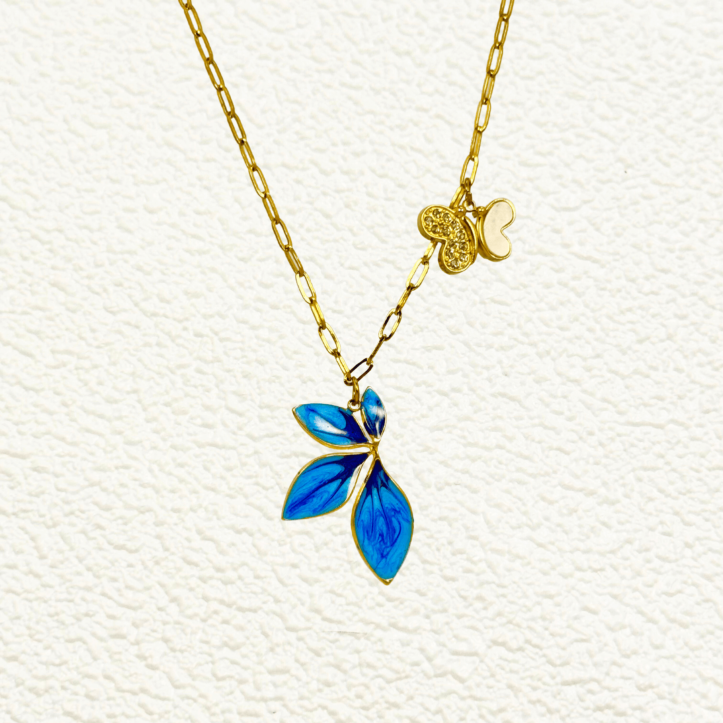 Gold charm necklace with blue enamel leaf, butterfly, and heart on waterproof paperclip chain