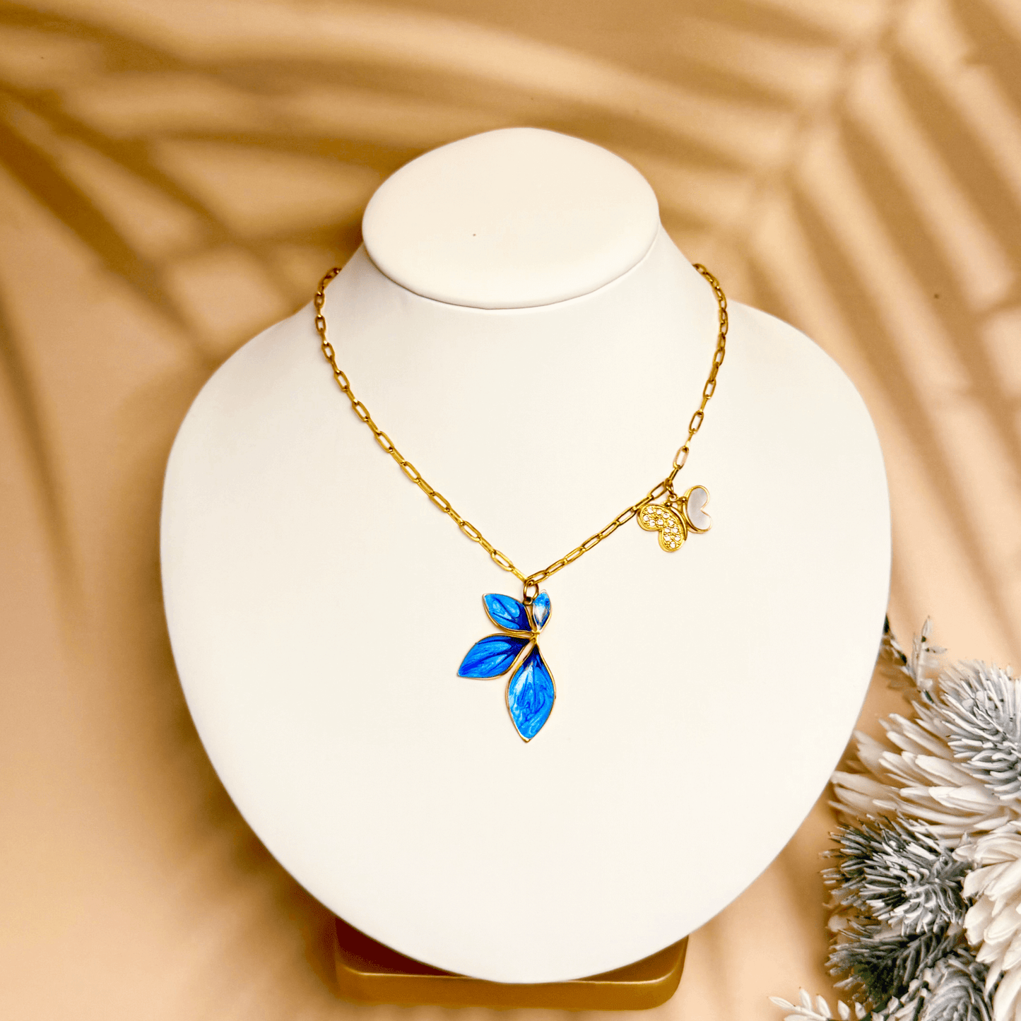 Gold charm necklace with blue enamel leaf, butterfly, and heart on waterproof paperclip chain