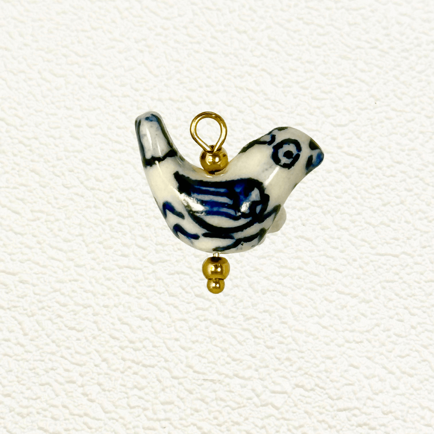 Hand-painted white ceramic charm in the shape of a bird with blue wing detailing and gold beads