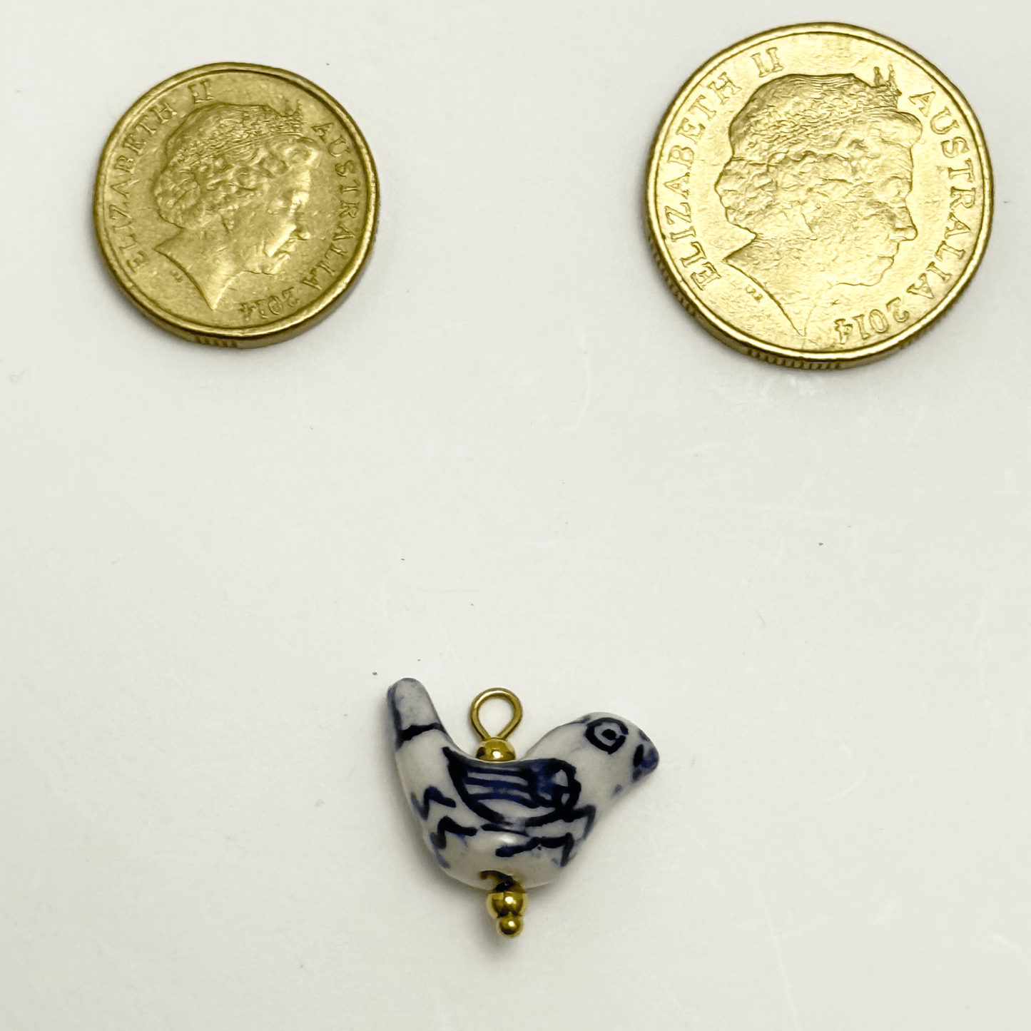 Hand-painted white ceramic charm in the shape of a bird with blue wing detailing and gold beads