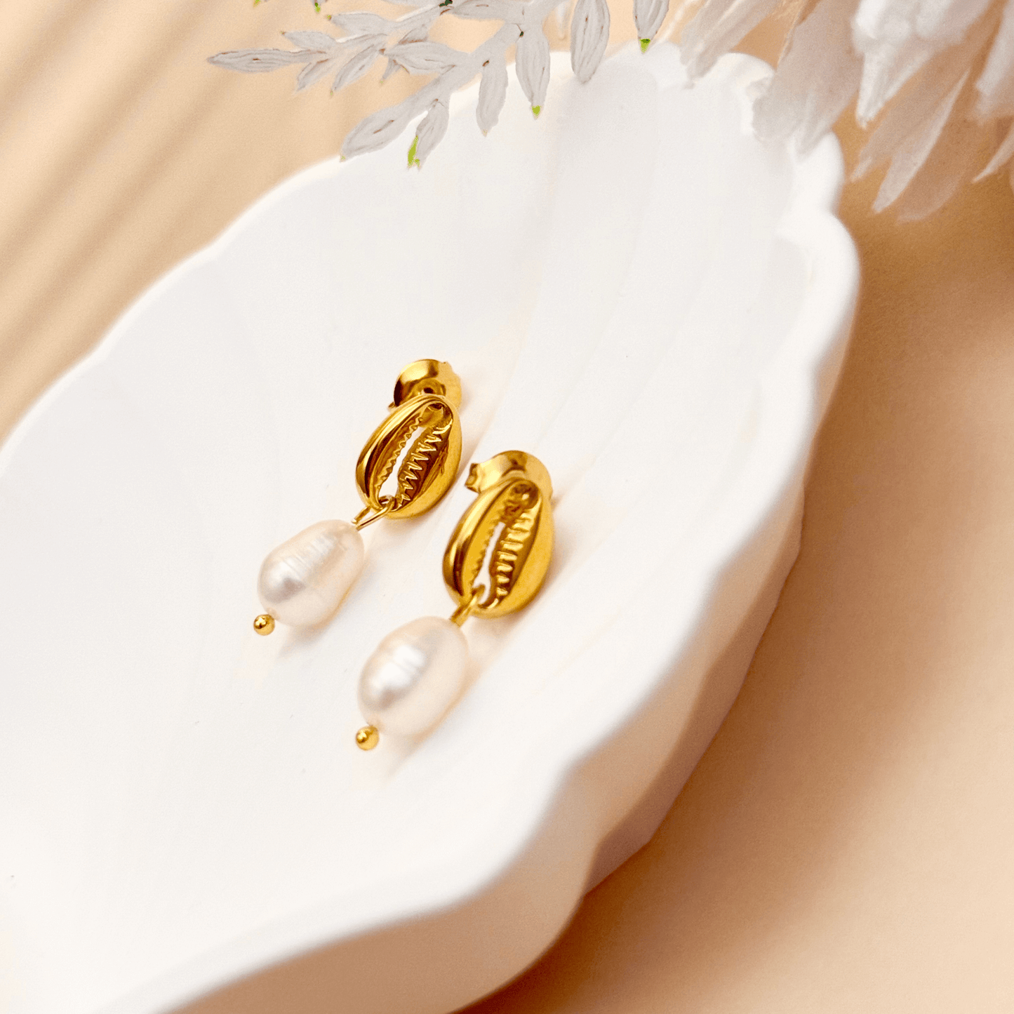 Gold cowrie shell earrings with freshwater pearl drops on white background