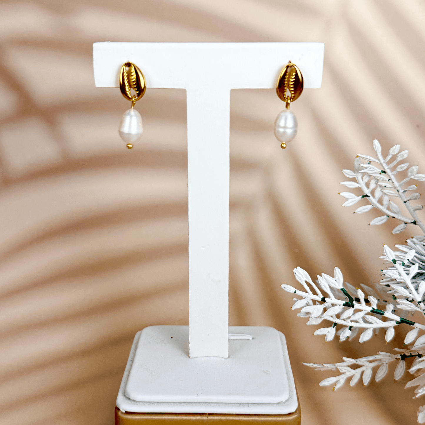 Gold cowrie shell earrings with freshwater pearl drops on white background