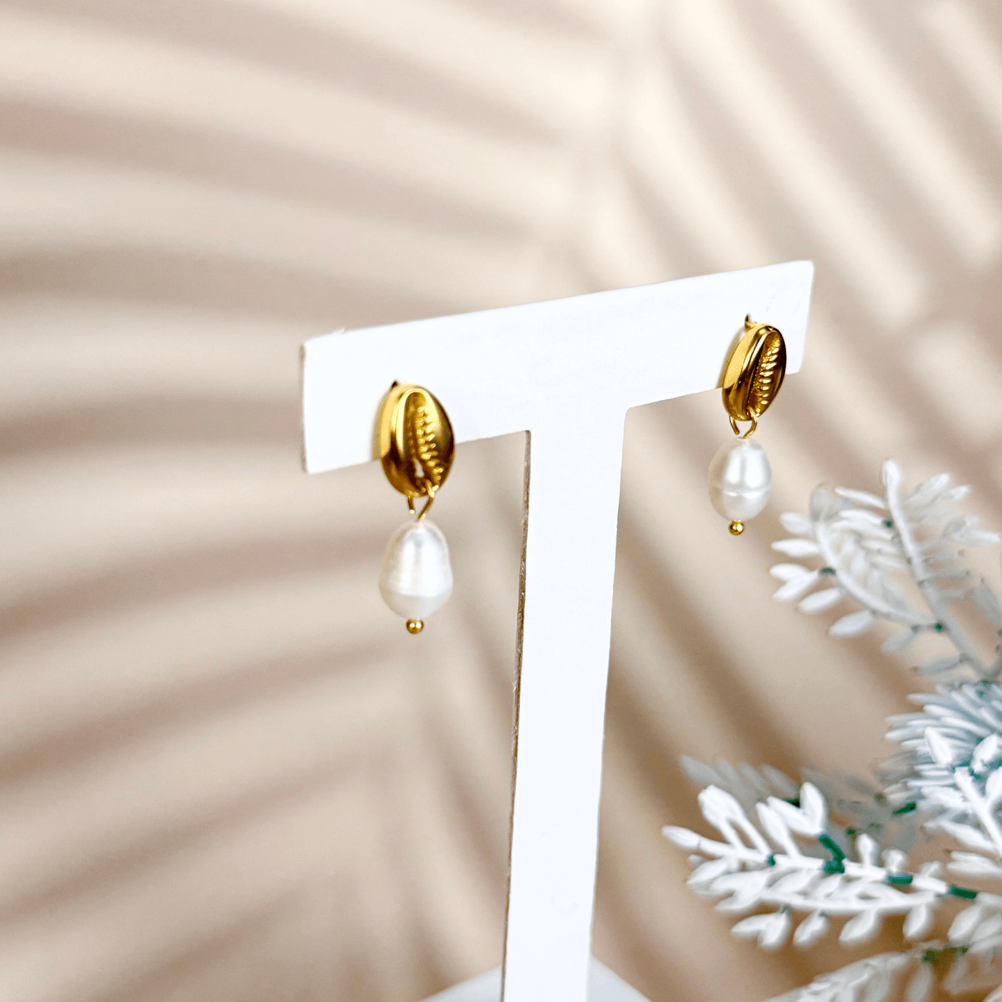 Gold cowrie shell earrings with freshwater pearl drops on white background