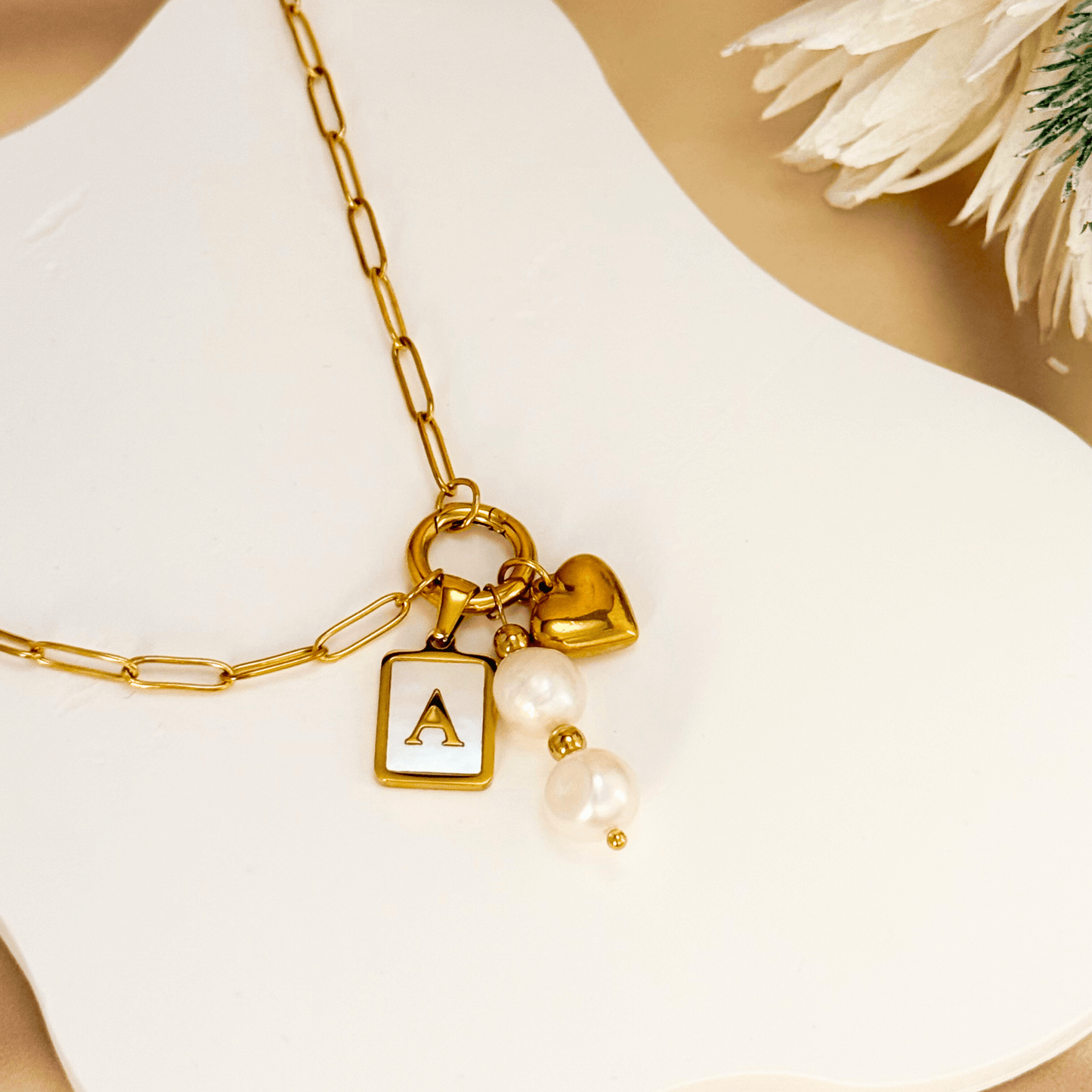 Gold paperclip chain necklace with customisable initial charm, heart pendant, and two freshwater pearls displayed on white bust.