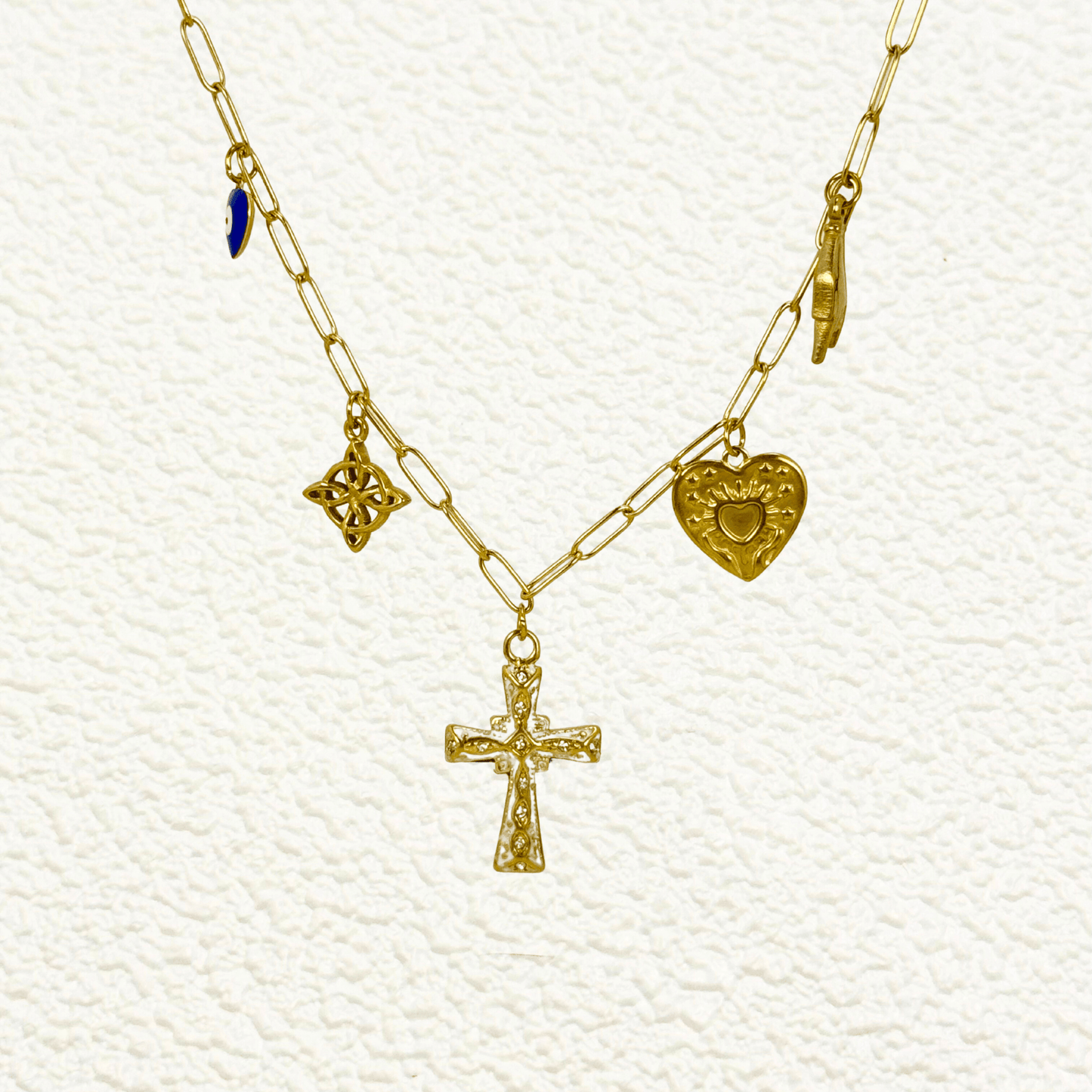 Gold charm necklace with cross, evil eye, sacred heart, hamsa hand, and Celtic knot on paperclip chain