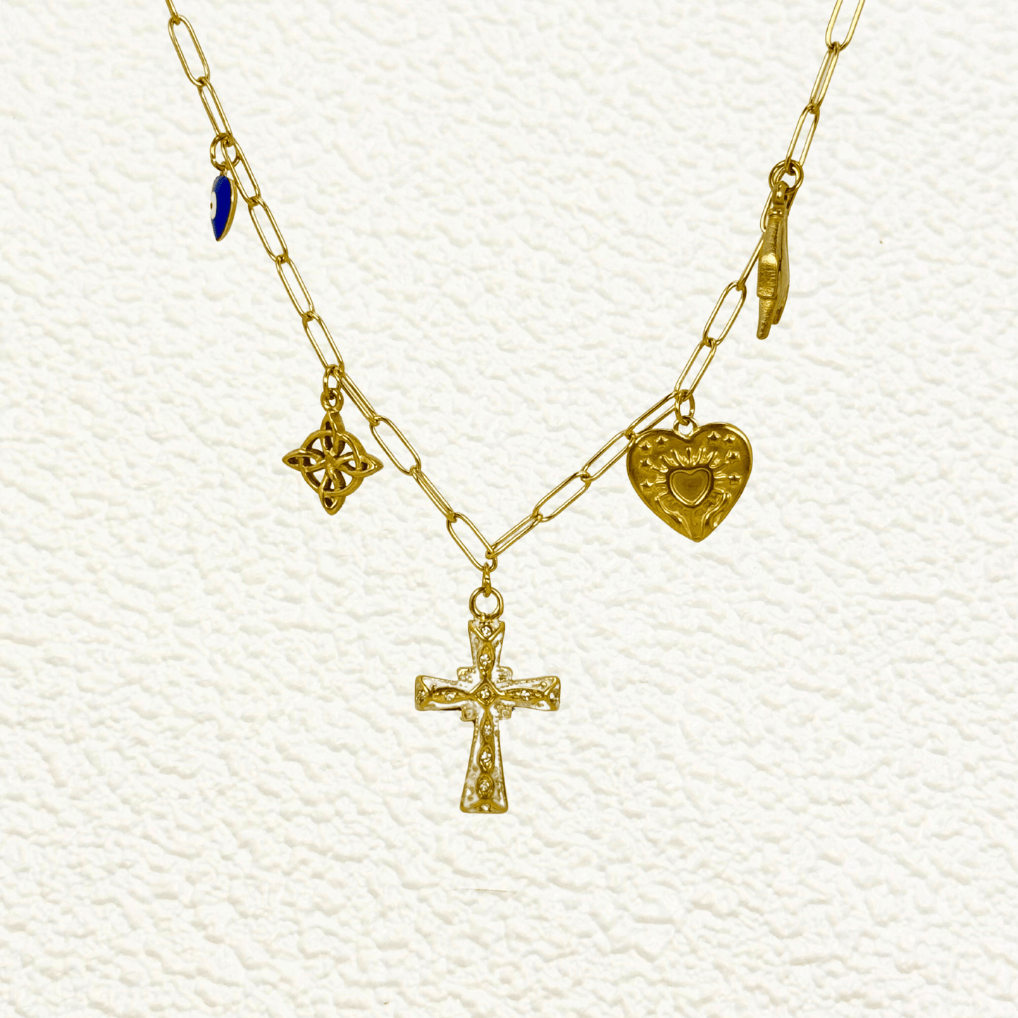 Gold charm necklace with cross, evil eye, sacred heart, hamsa hand, and Celtic knot on paperclip chain