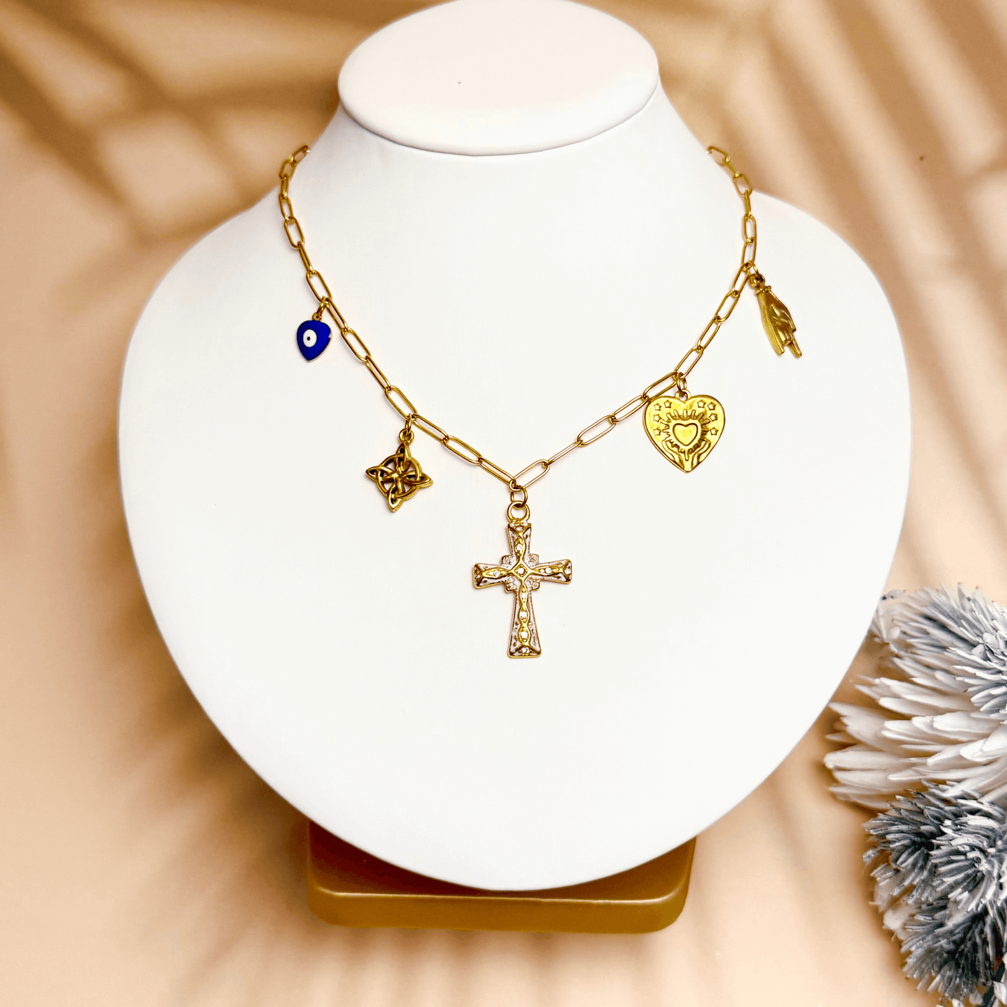 Gold charm necklace with cross, evil eye, sacred heart, hamsa hand, and Celtic knot on paperclip chain