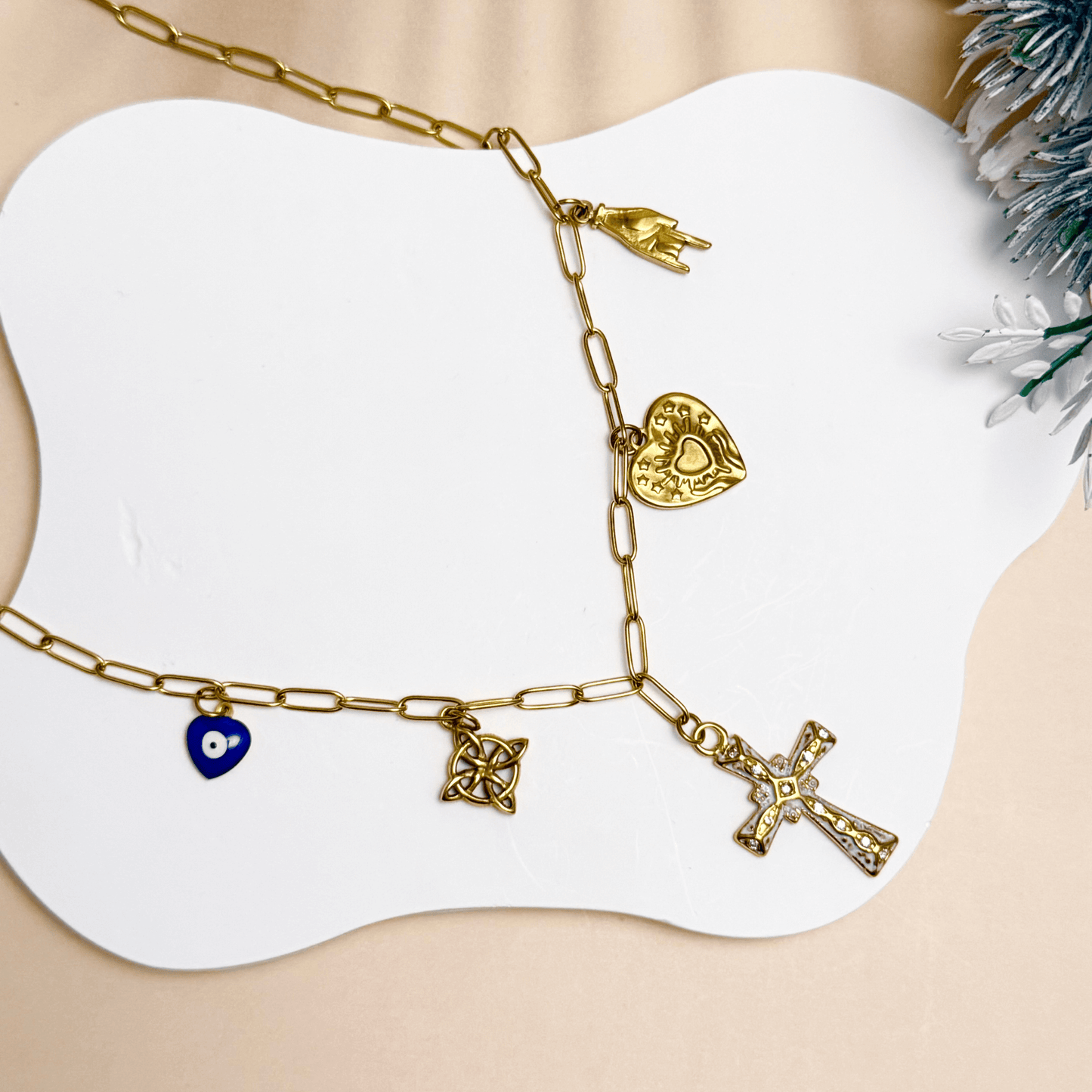 Gold charm necklace with cross, evil eye, sacred heart, hamsa hand, and Celtic knot on paperclip chain