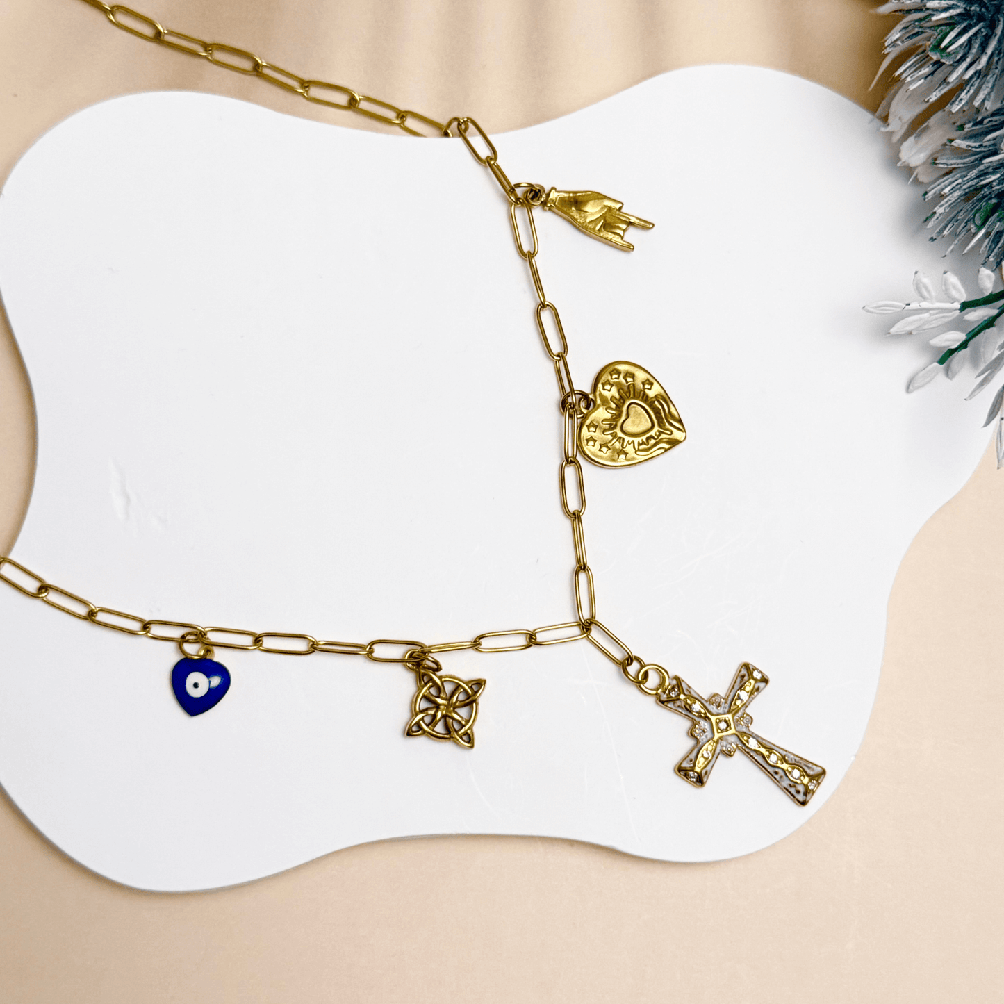 Gold charm necklace with cross, evil eye, sacred heart, hamsa hand, and Celtic knot on paperclip chain