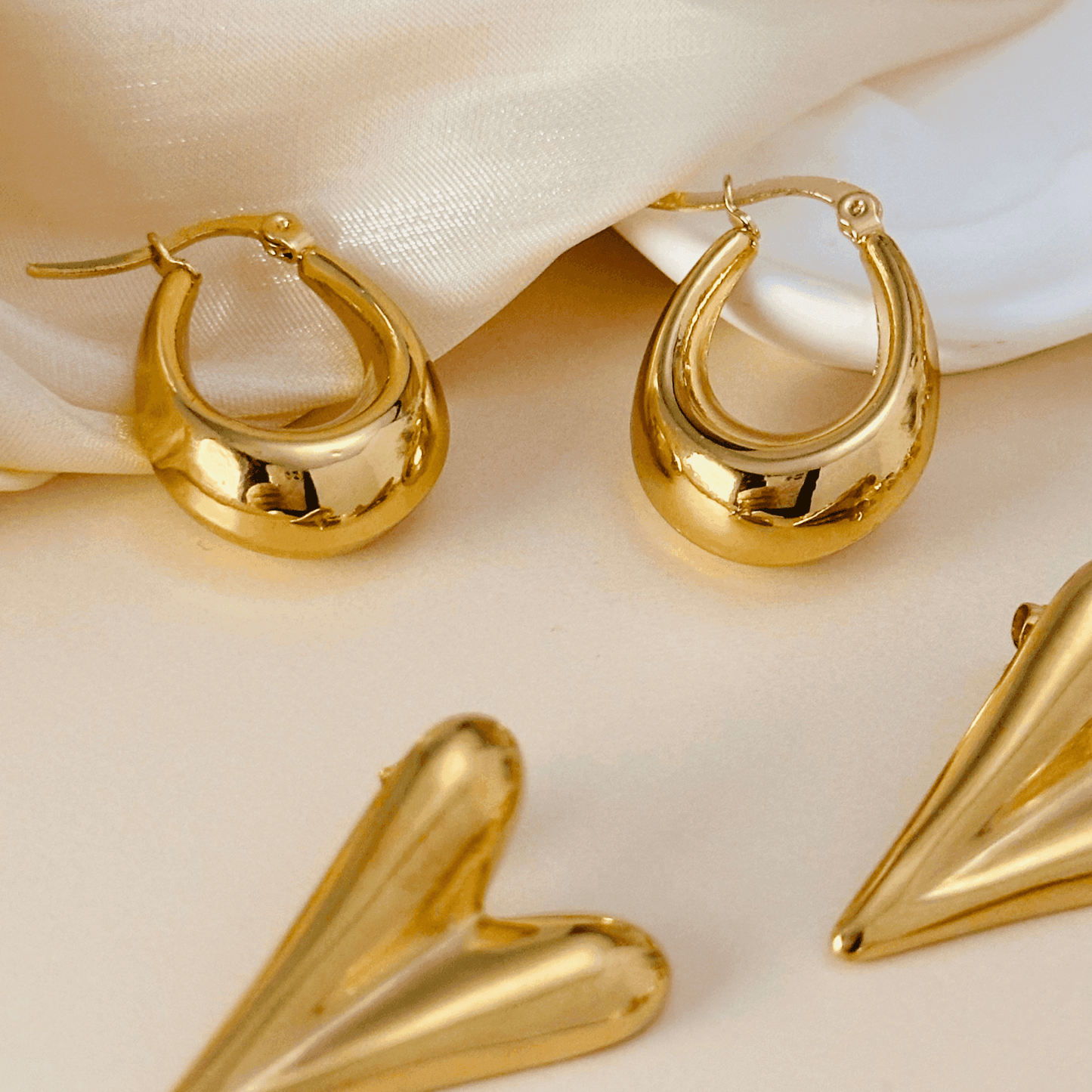 A collection of gold earrings featuring bold, modern, and pearl-accented designs, including hoops, hearts, and sculptural styles. Perfect for statement and elegant looks.