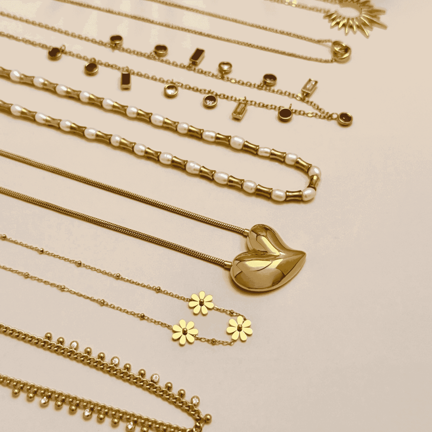 A stylish collection of gold-plated necklaces, including pearl accents, sculpted heart pendant, celestial sun charm, and daisy floral designs, elegantly stacked for a modern layered look.