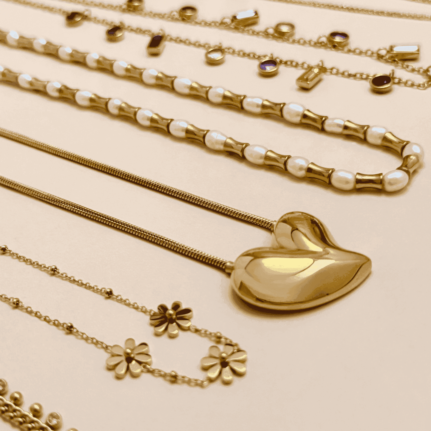 A stylish collection of gold-plated necklaces, including pearl accents, sculpted heart pendant, celestial sun charm, and daisy floral designs, elegantly stacked for a modern layered look.