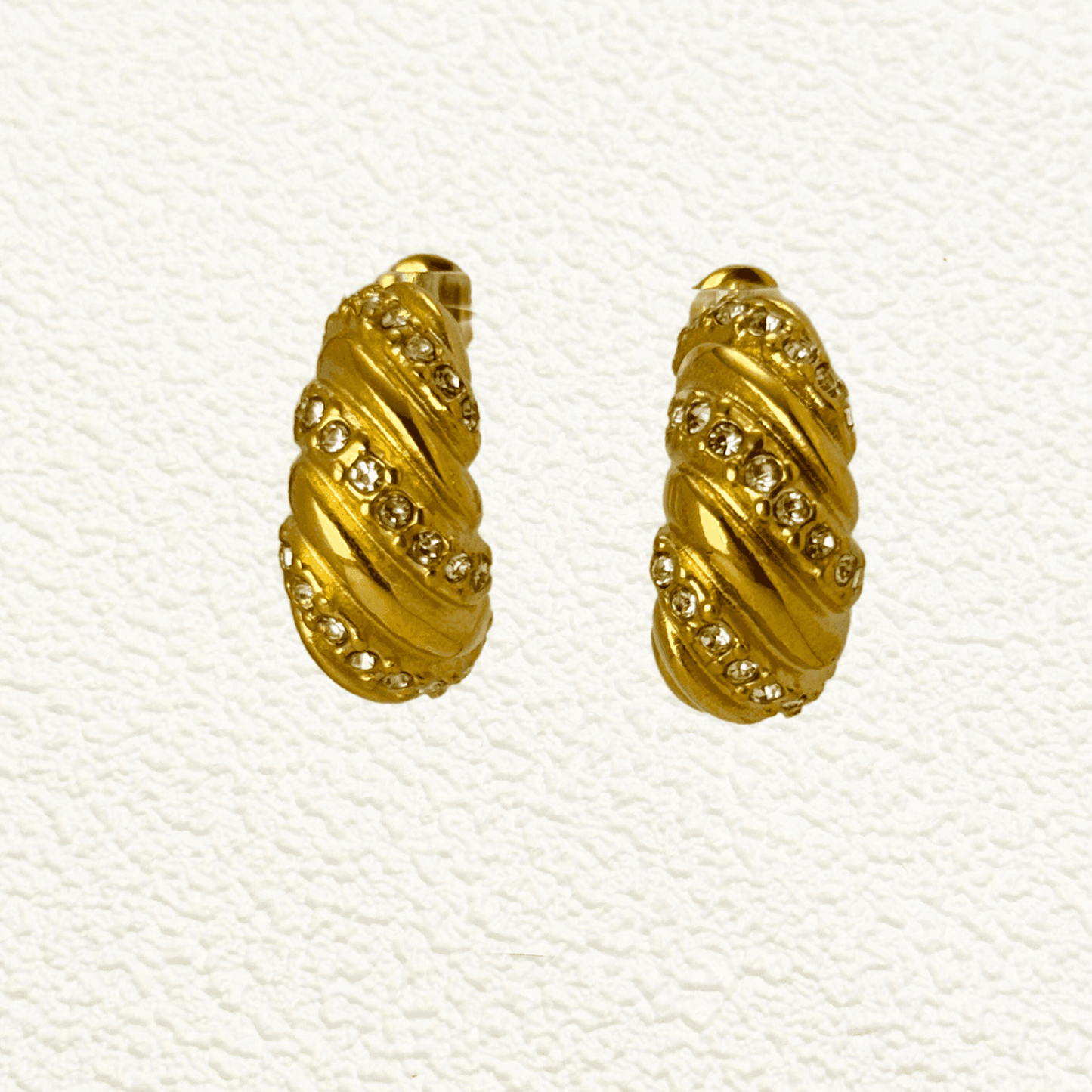 Gold-tone twisted hoop earrings with a sculptural, textured design, featuring embedded zircon stones. Crafted from stainless steel with a waterproof PVD coating, these earrings offer a bold yet elegant statement. Secure latch-back closure for a comfortable fit