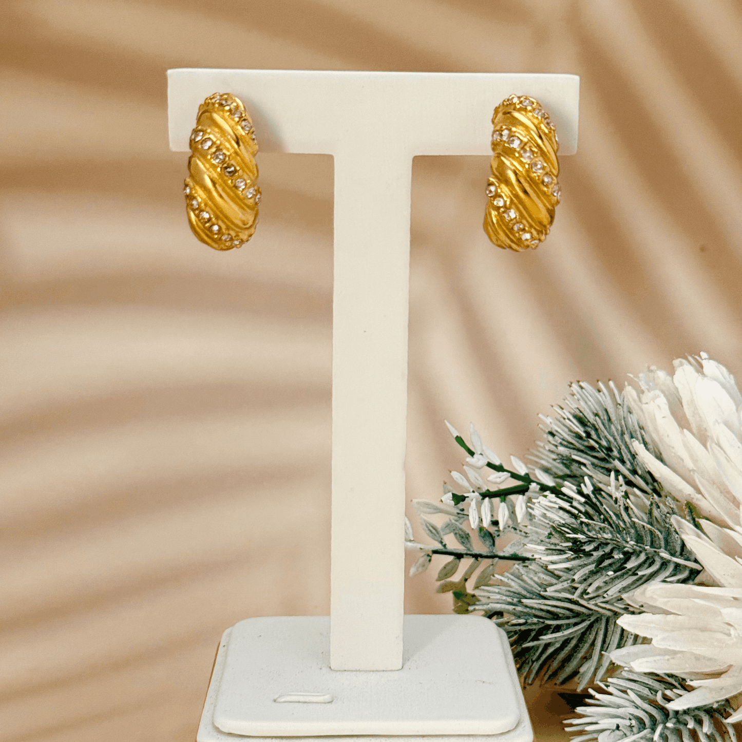 Gold-tone twisted hoop earrings with a sculptural, textured design, featuring embedded zircon stones. Crafted from stainless steel with a waterproof PVD coating, these earrings offer a bold yet elegant statement. Secure latch-back closure for a comfortable fit