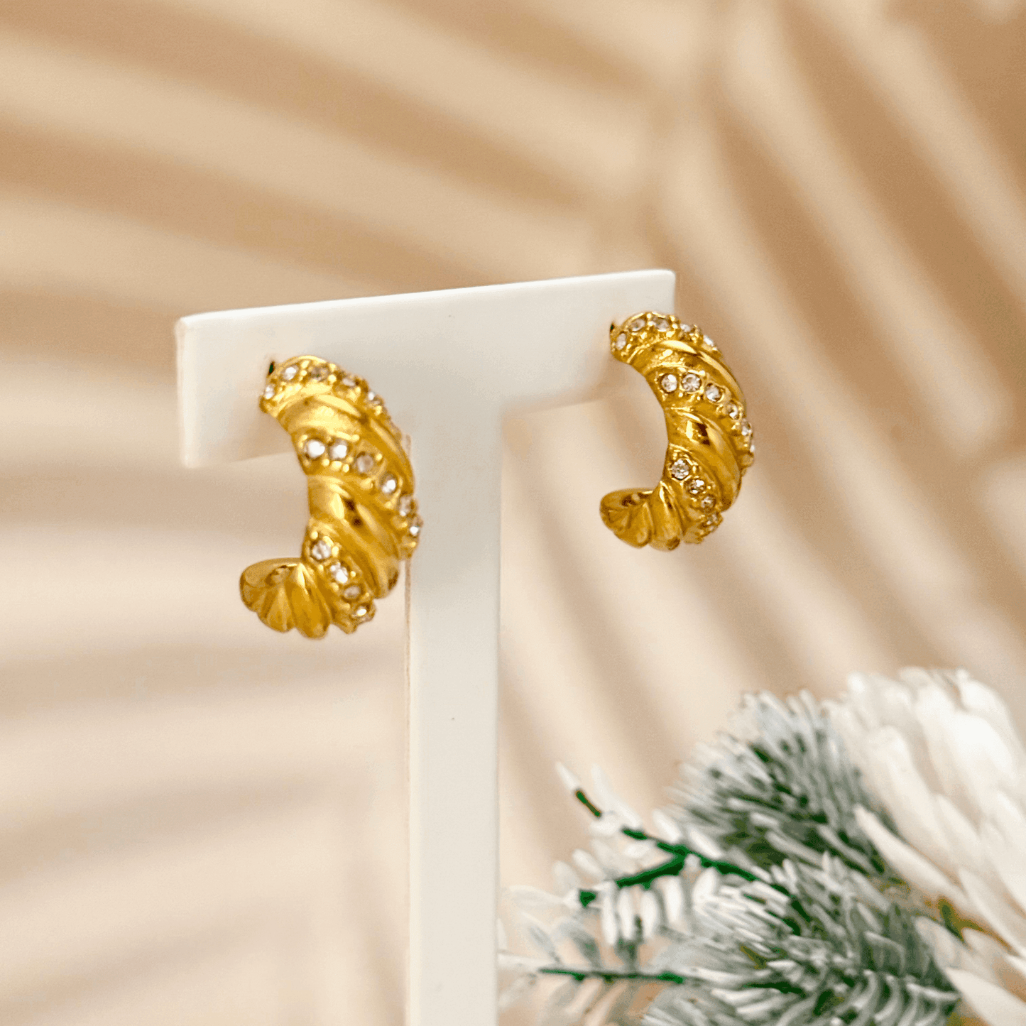 Gold-tone twisted hoop earrings with a sculptural, textured design, featuring embedded zircon stones. Crafted from stainless steel with a waterproof PVD coating, these earrings offer a bold yet elegant statement. Secure latch-back closure for a comfortable fit