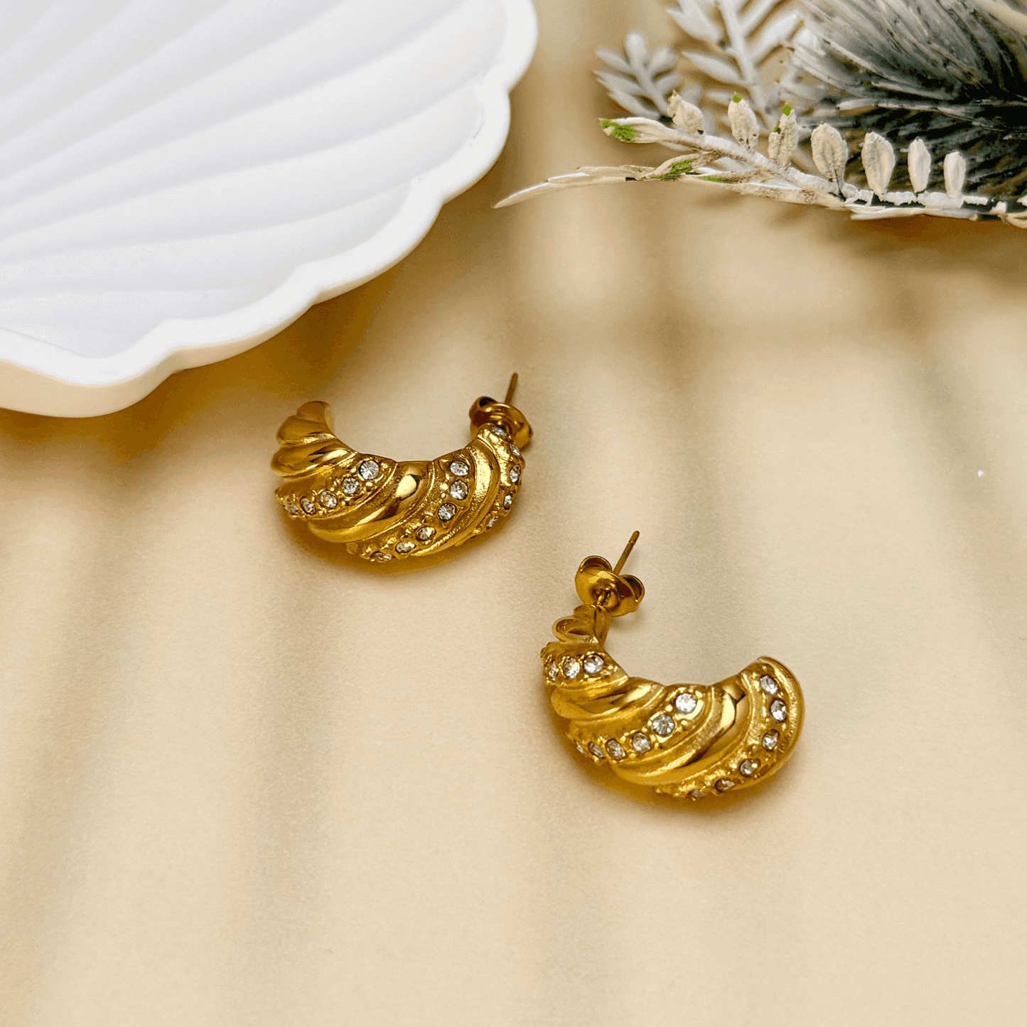 Gold-tone twisted hoop earrings with a sculptural, textured design, featuring embedded zircon stones. Crafted from stainless steel with a waterproof PVD coating, these earrings offer a bold yet elegant statement. Secure latch-back closure for a comfortable fit