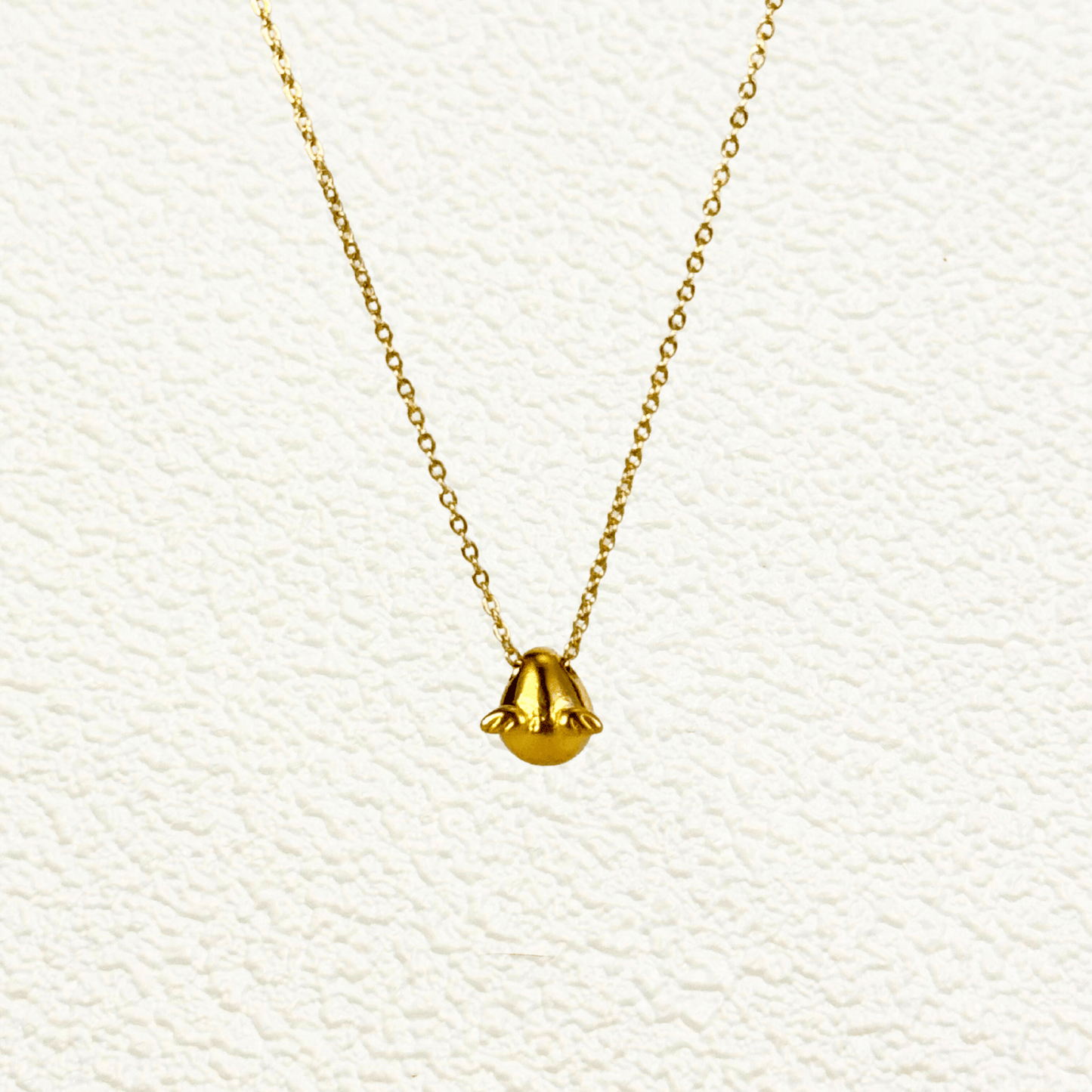 Gold charm necklace with a teardrop-shaped halo charm and small angel wing details, attached to a fine cable chain.