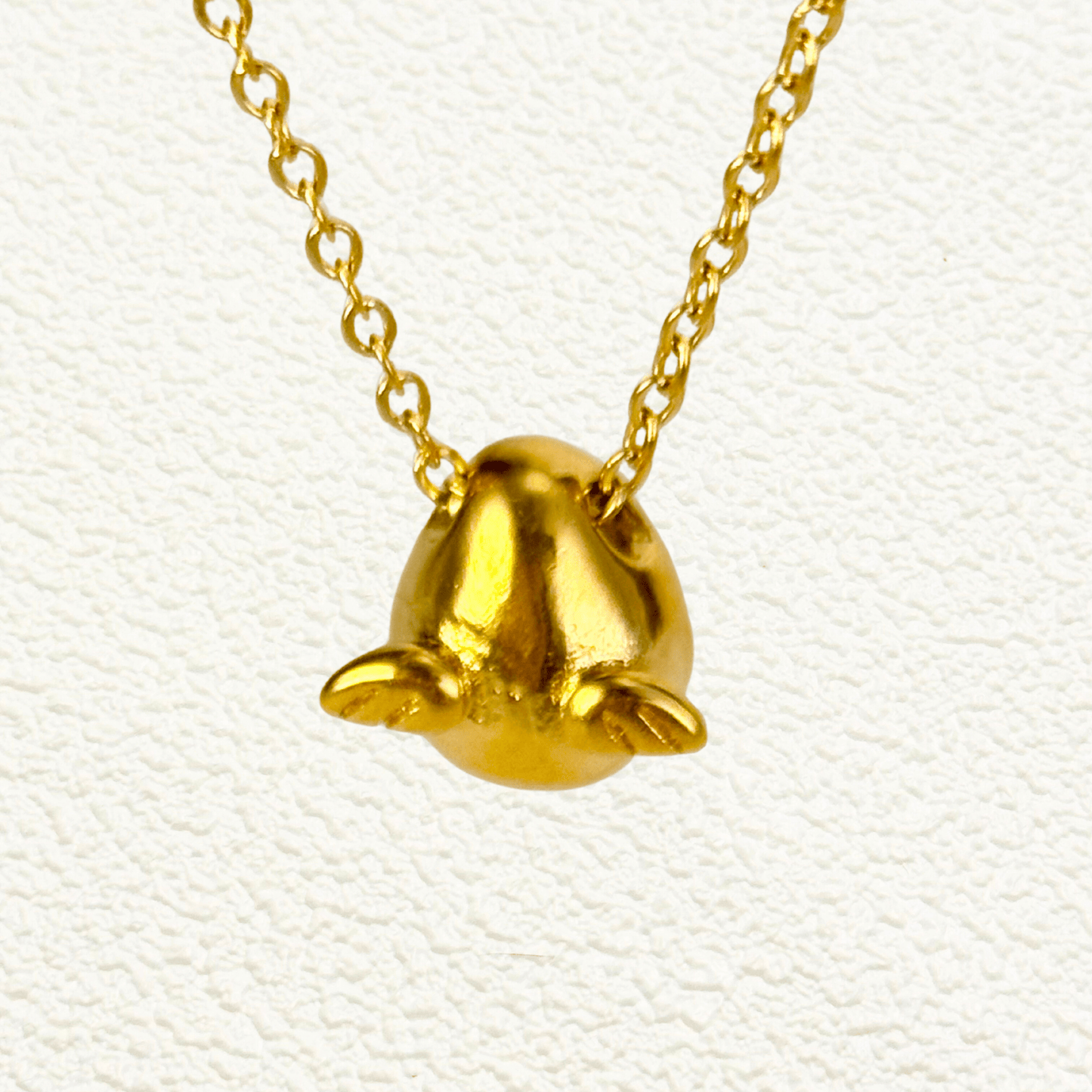 Gold charm necklace with a teardrop-shaped halo charm and small angel wing details, attached to a fine cable chain.