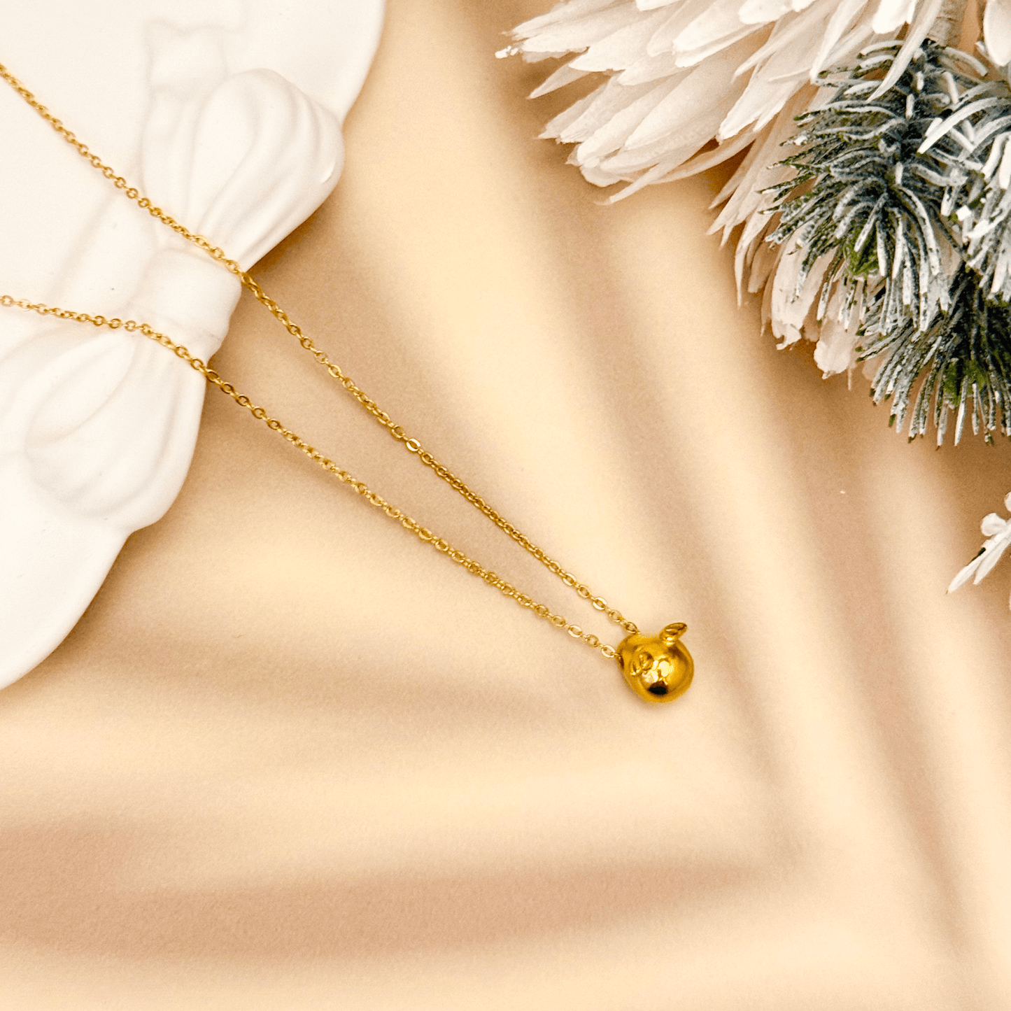 Gold charm necklace with a teardrop-shaped halo charm and small angel wing details, attached to a fine cable chain.