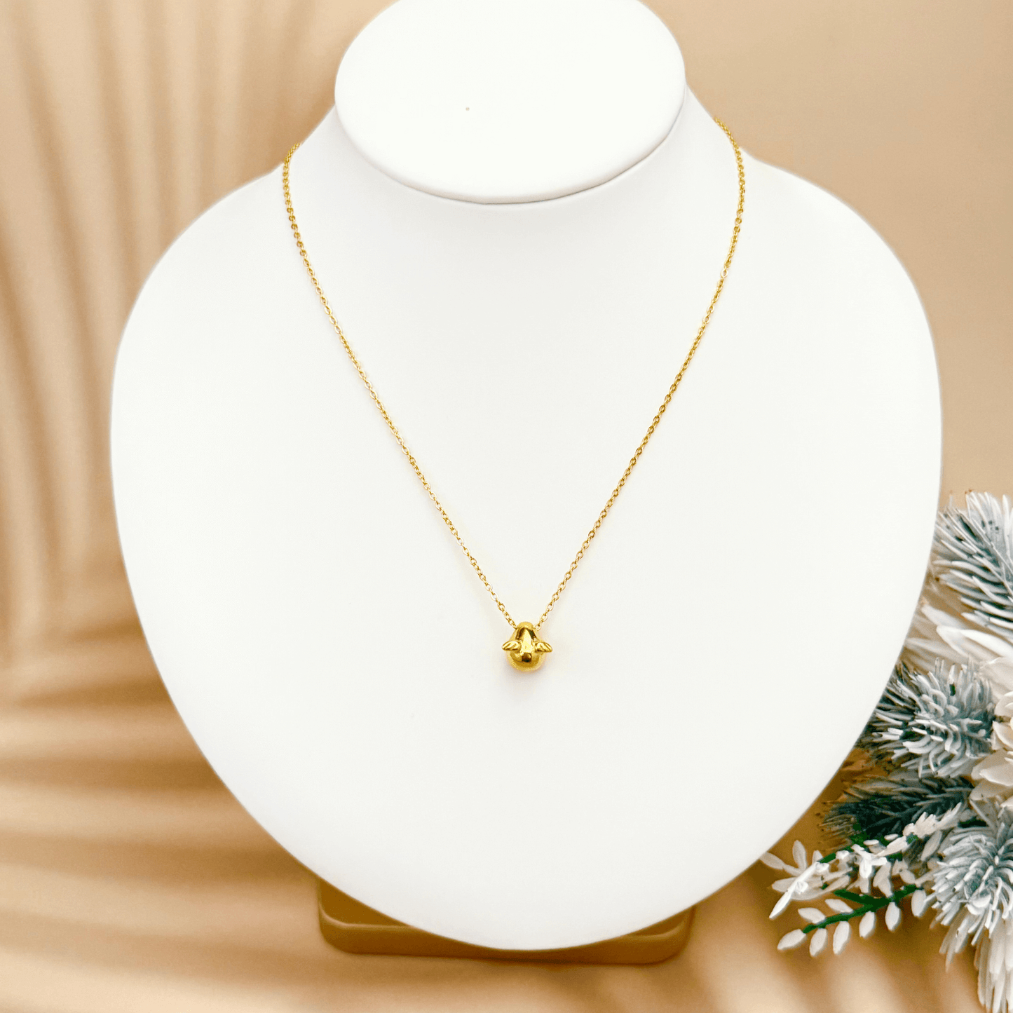 Gold charm necklace with a teardrop-shaped halo charm and small angel wing details, attached to a fine cable chain.