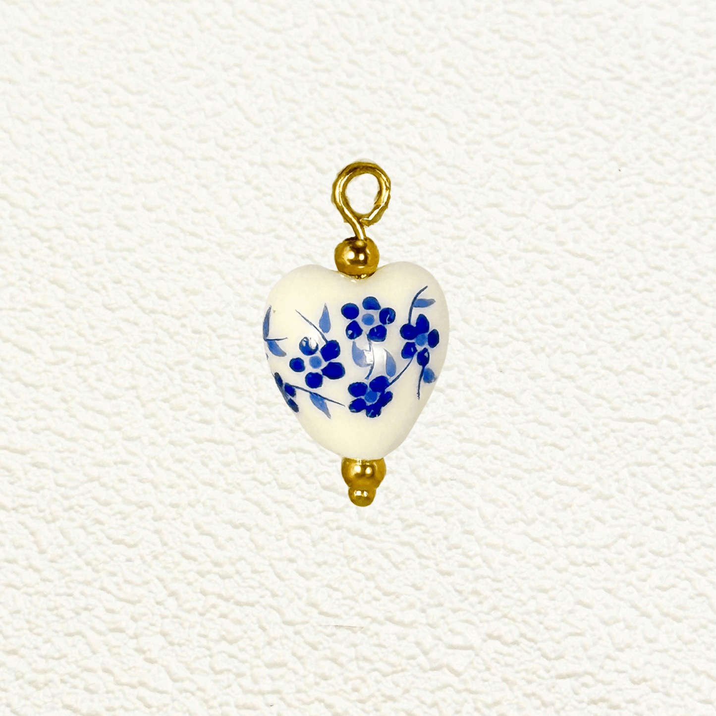 Heart-shaped ceramic charm with small blue flowers and gold bead details