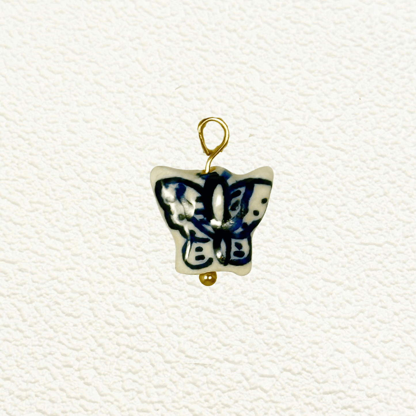 Blue and white ceramic butterfly charm with abstract wing patterns and gold loop