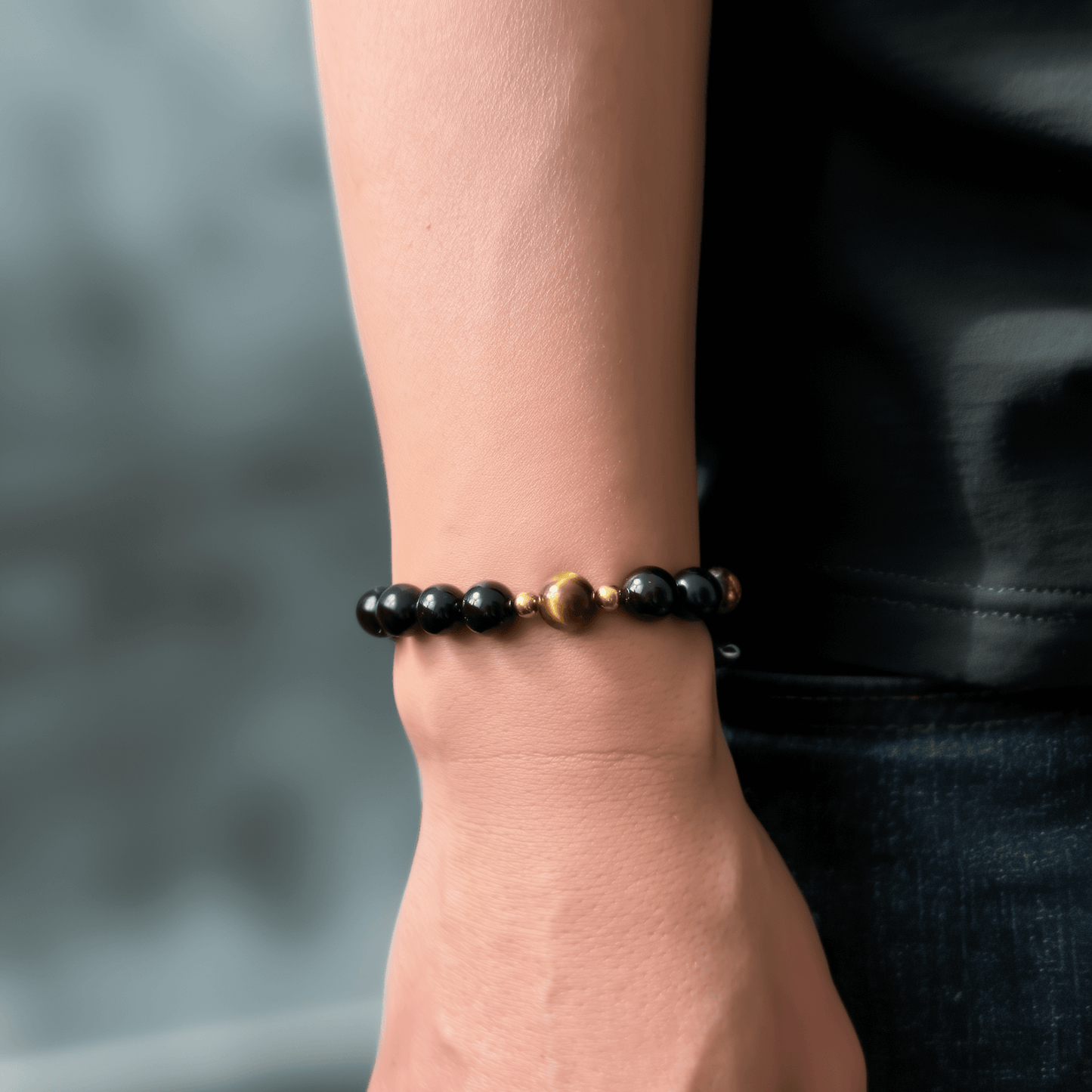 Men’s bracelet with polished black agate beads, single tiger’s eye gemstone, and gold accents on stretch cord.