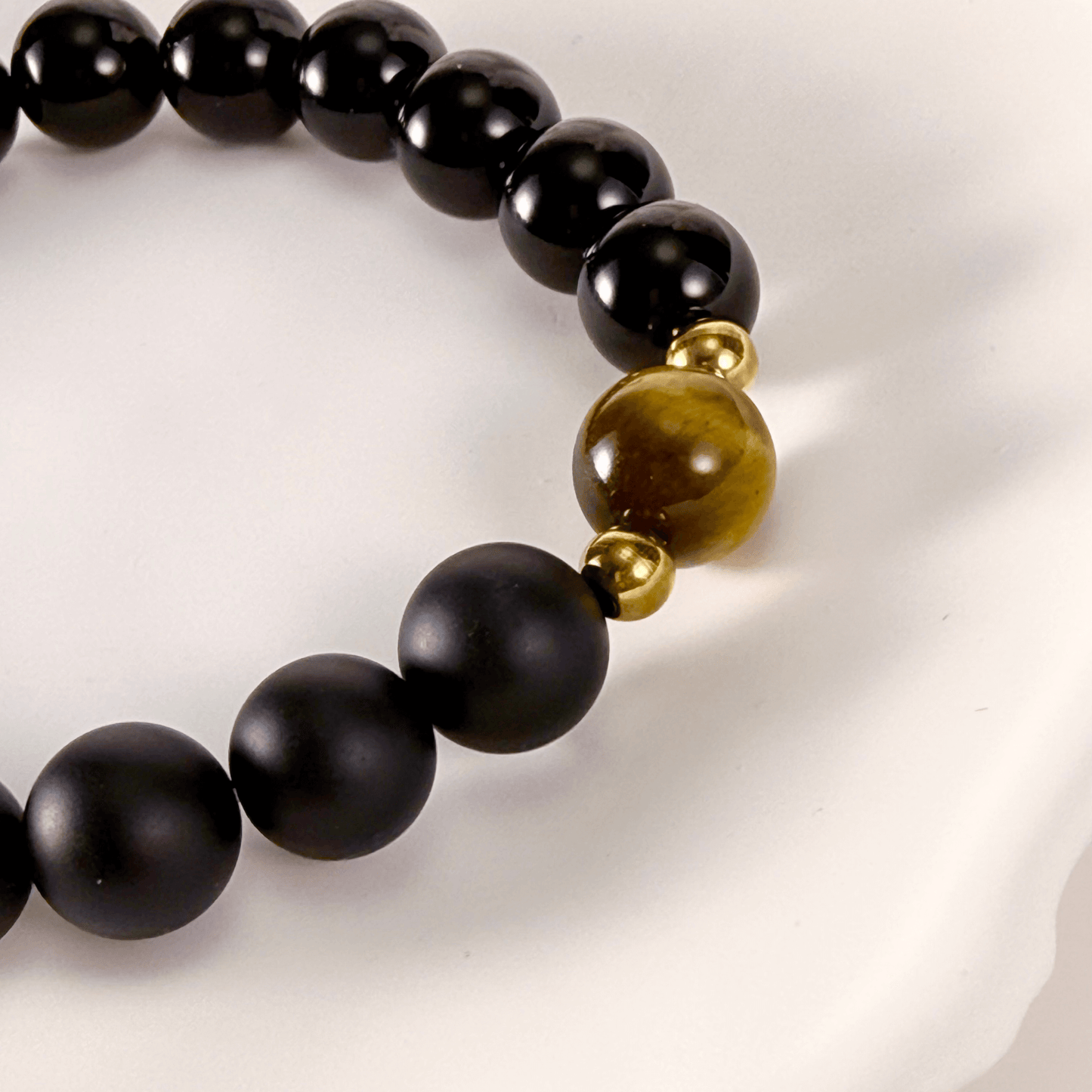 Men’s bracelet with polished black agate beads, single tiger’s eye gemstone, and gold accents on stretch cord.