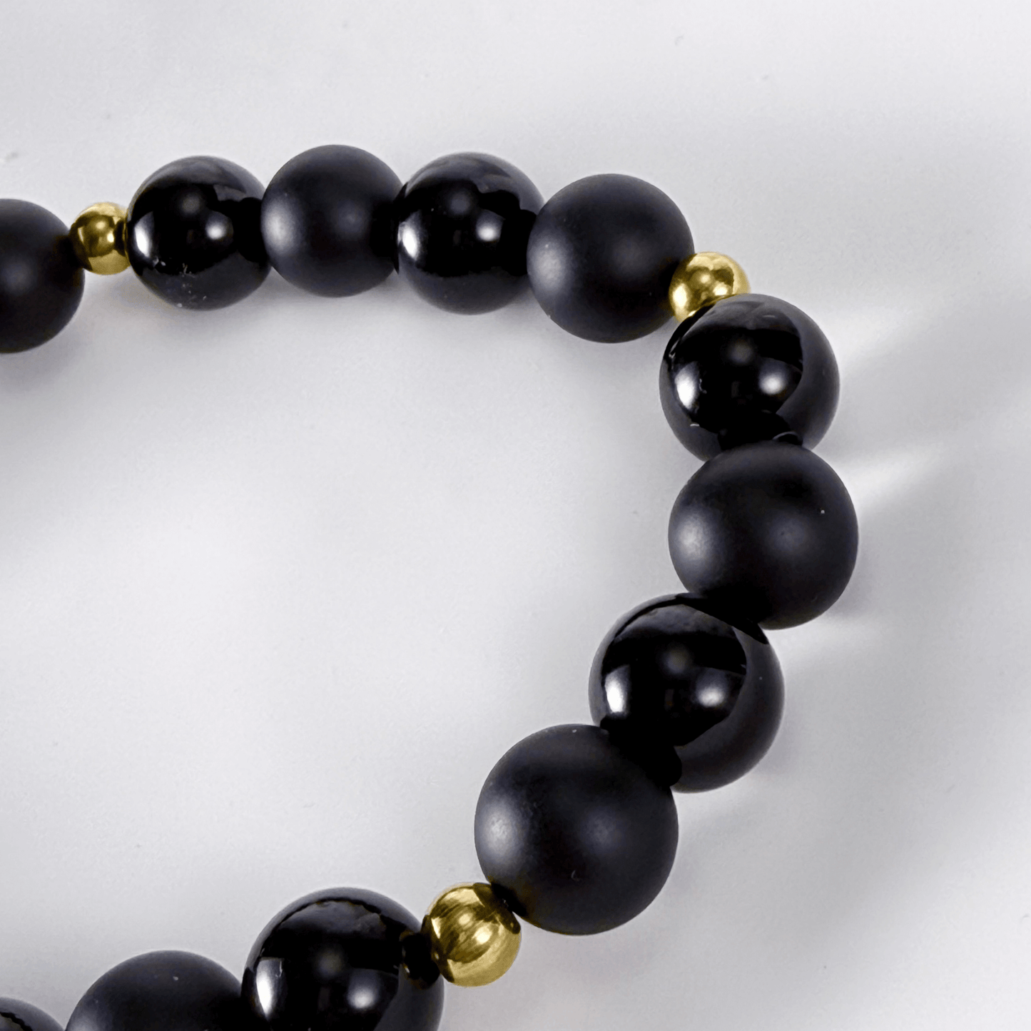 Men’s two-tone bracelet with matte and polished black agate gemstone beads, accented by gold spacers on stretch cord.