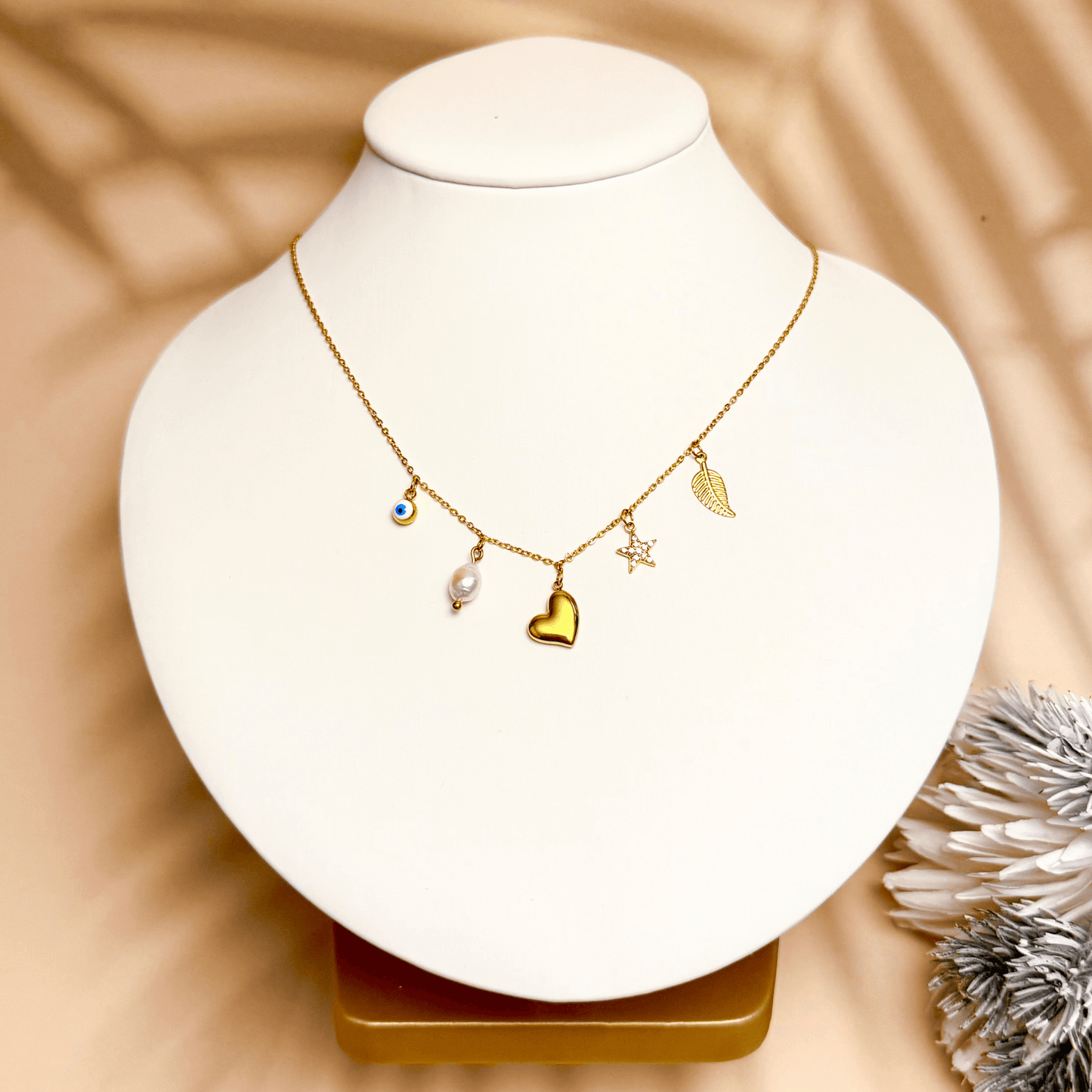 Mini gold charm necklace with evil eye, heart, pearl, star, and leaf on waterproof chain