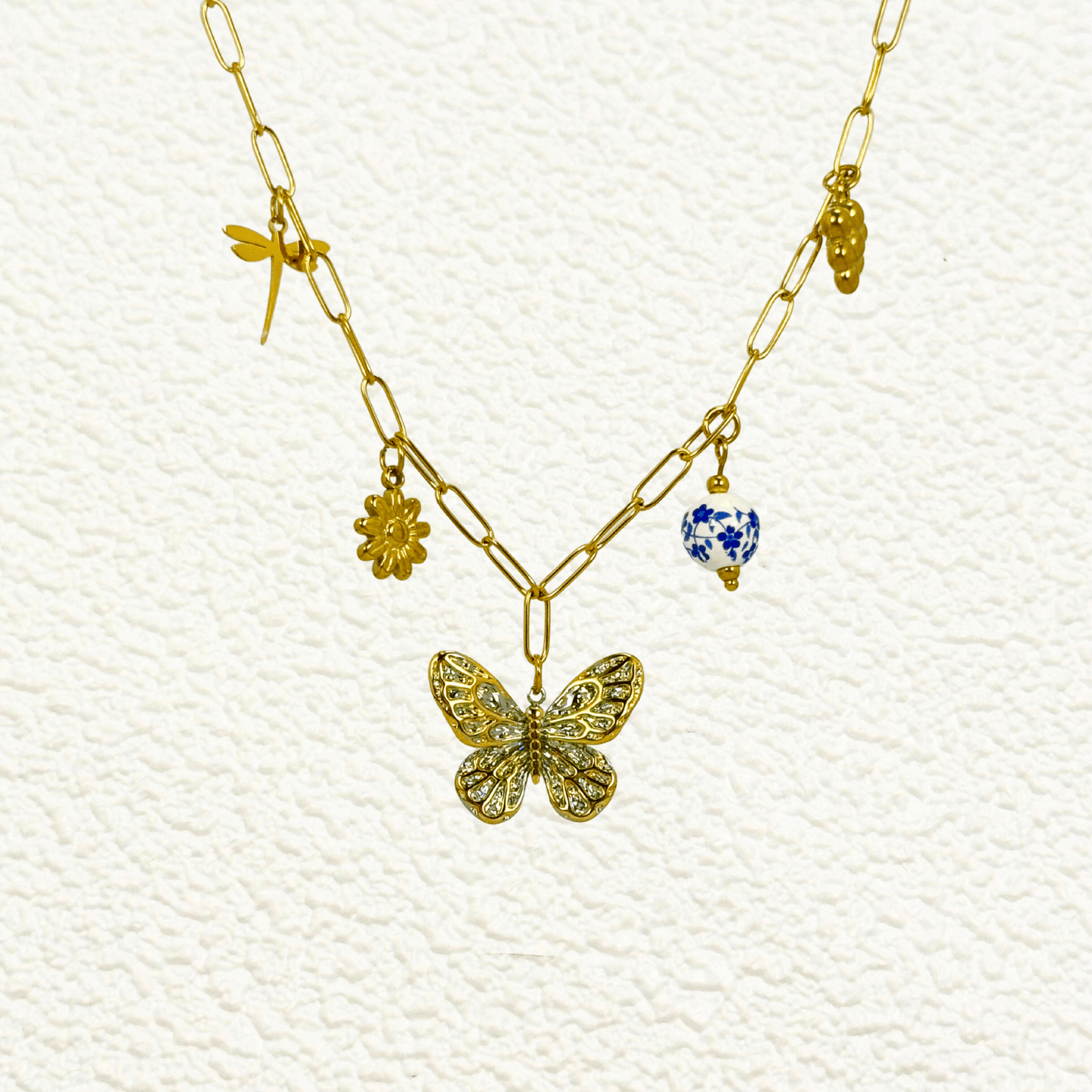 Gold charm necklace with butterfly, daisy, dragonfly, grape, and blue floral bead on waterproof paperclip chain
