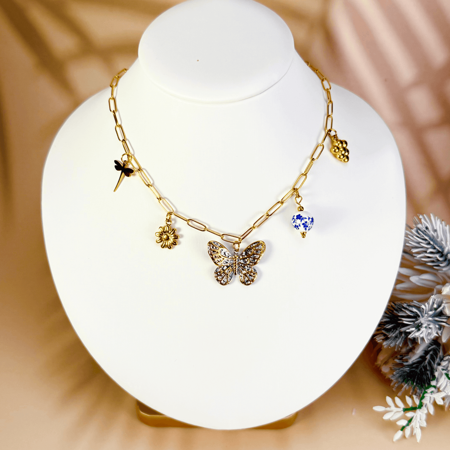 Gold charm necklace with butterfly, daisy, dragonfly, grape, and blue floral bead on waterproof paperclip chain