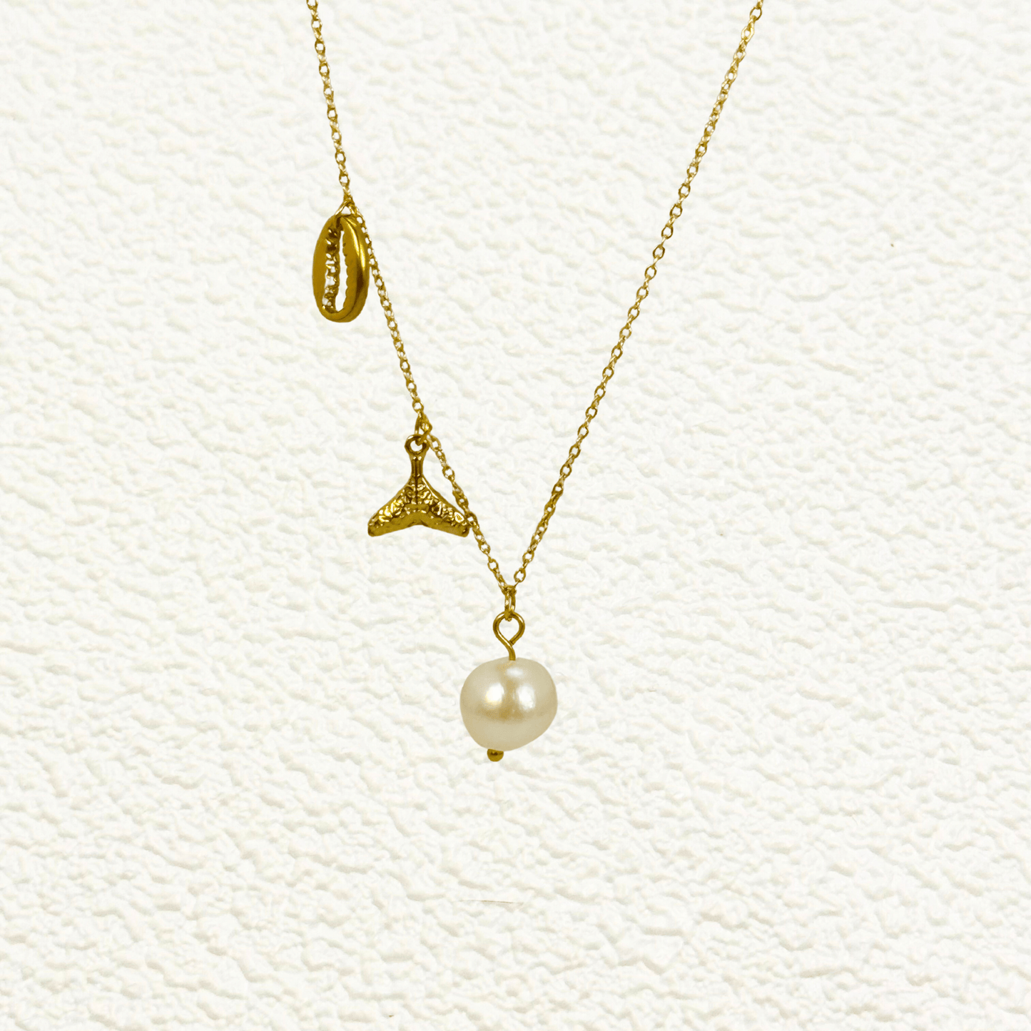 Gold necklace with pearl, whale tail, and shell charms on dainty waterproof chain