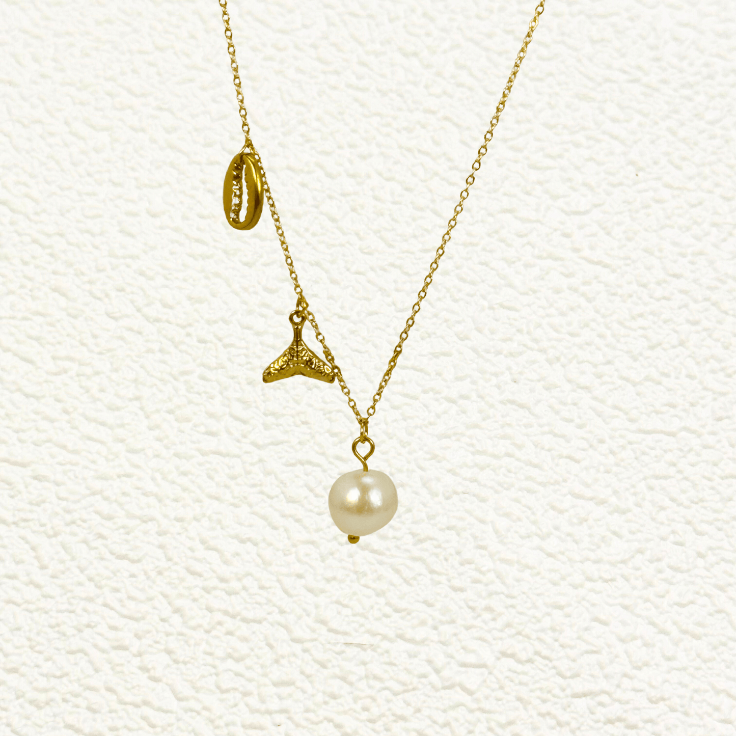 Gold necklace with pearl, whale tail, and shell charms on dainty waterproof chain