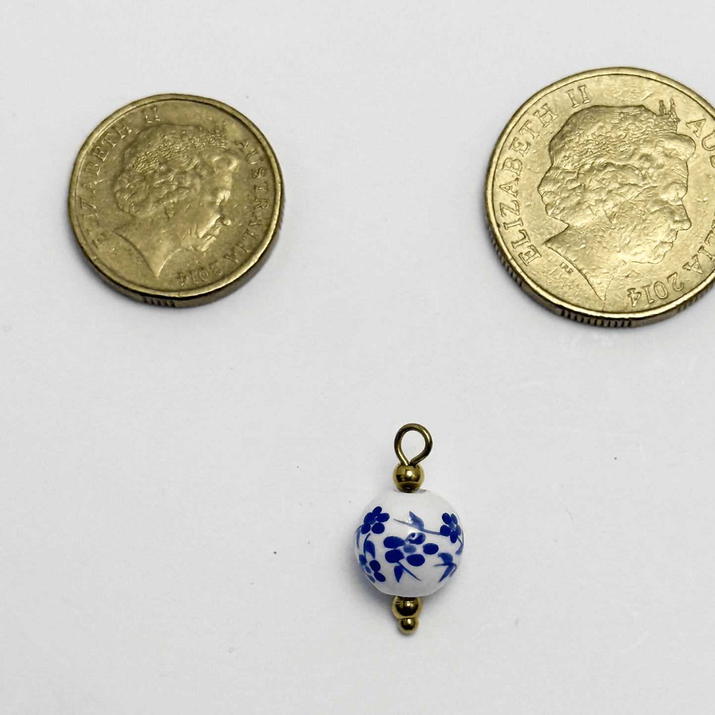 Round white ceramic charm with delicate blue flower and vine pattern, finished with gold accents
