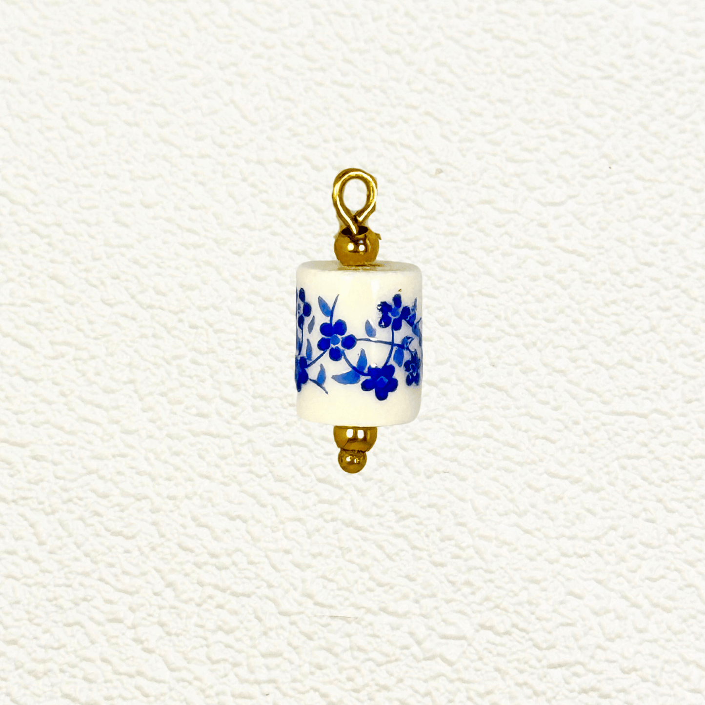 Cylindrical white ceramic charm with blue floral design and gold detailing