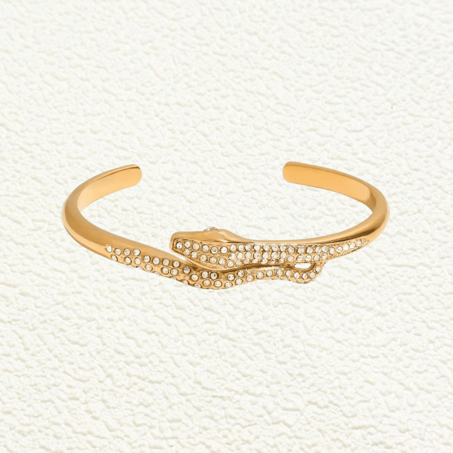Gold open cuff bracelet with snake design and zircon stones, shown alone and on wrist.