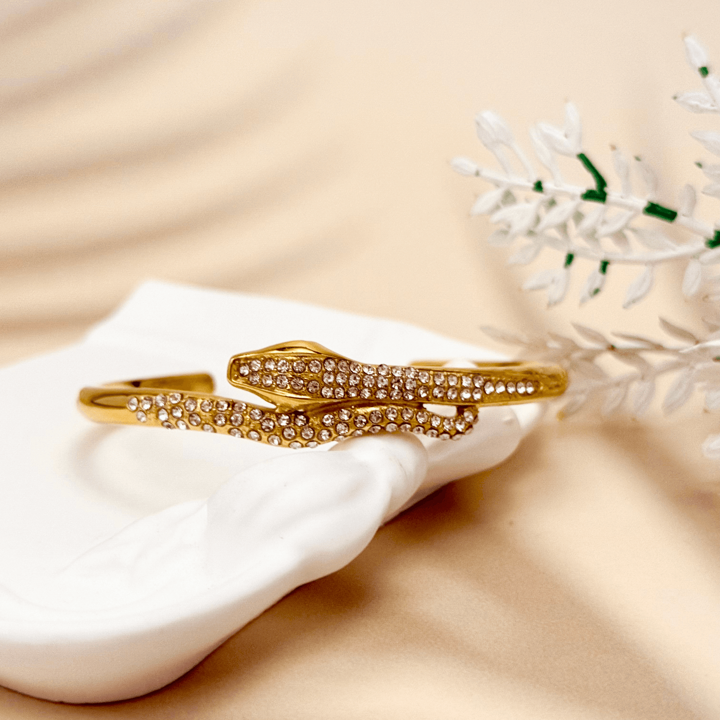 Gold open cuff bracelet with snake design and zircon stones, shown alone and on wrist.