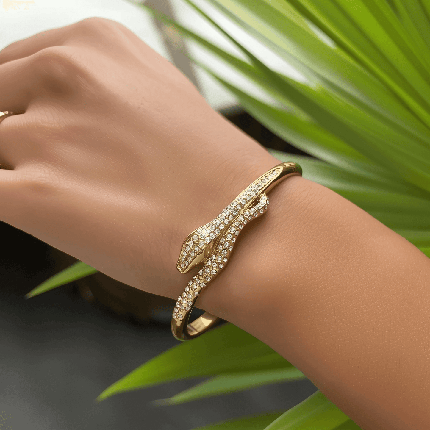 Gold open cuff bracelet with snake design and zircon stones, shown alone and on wrist.