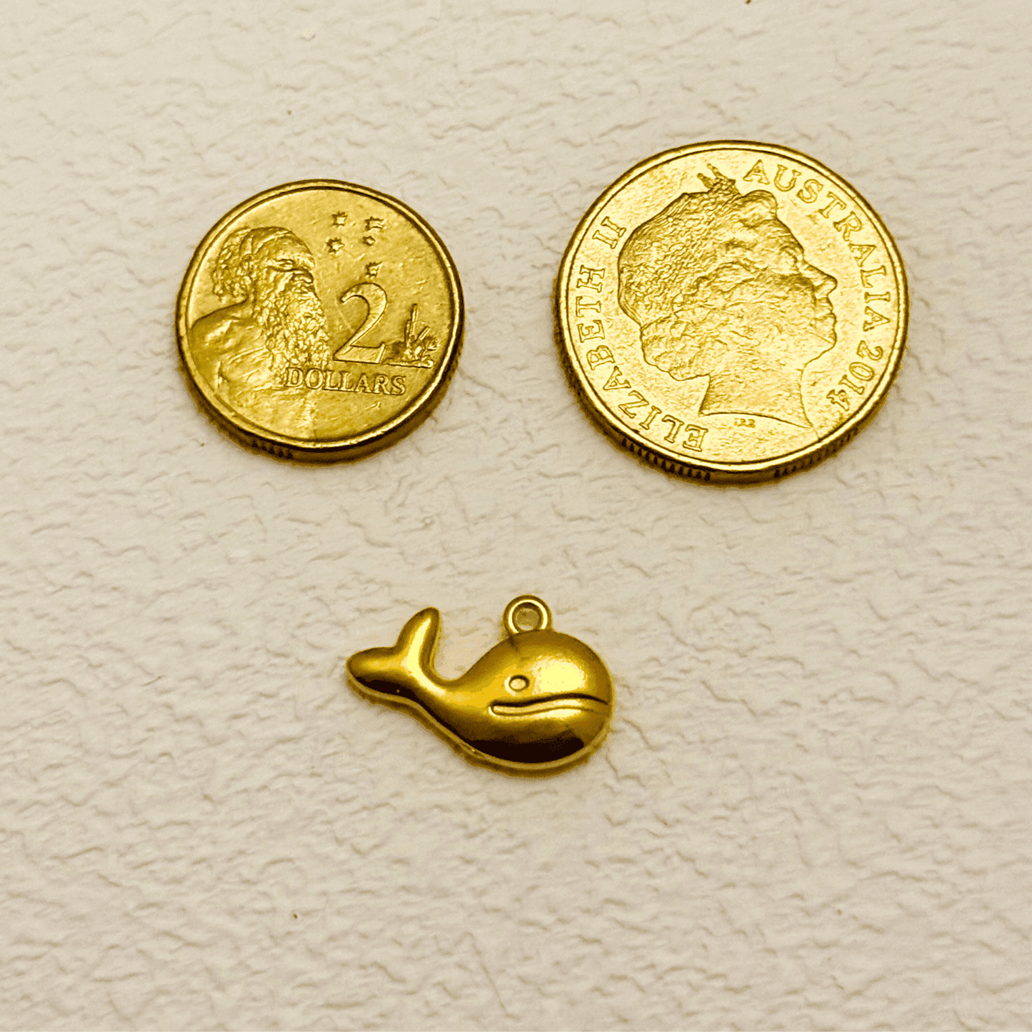 Gold whale charm with a smiling face and curved tail, PVD gold plated finish