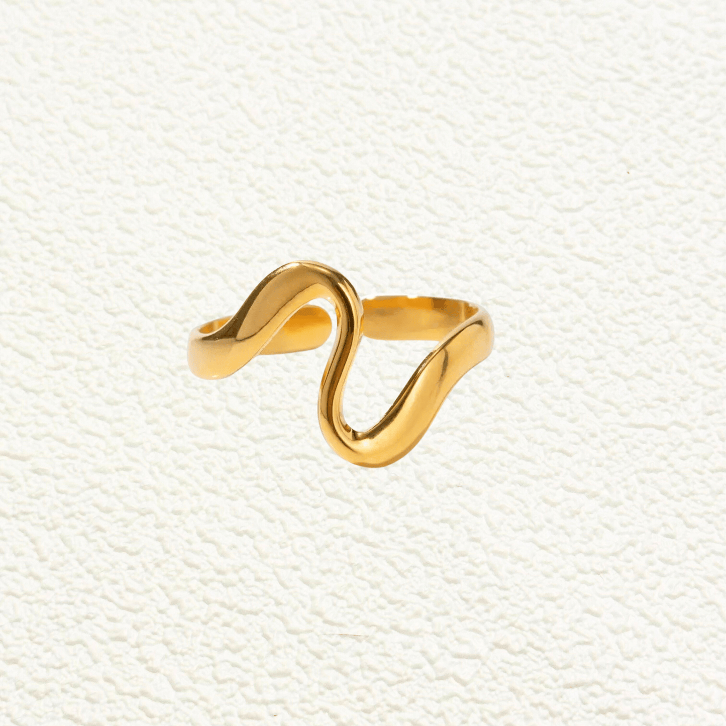 Gold minimalist open ring with soft wave-shaped design on white ceramic background.