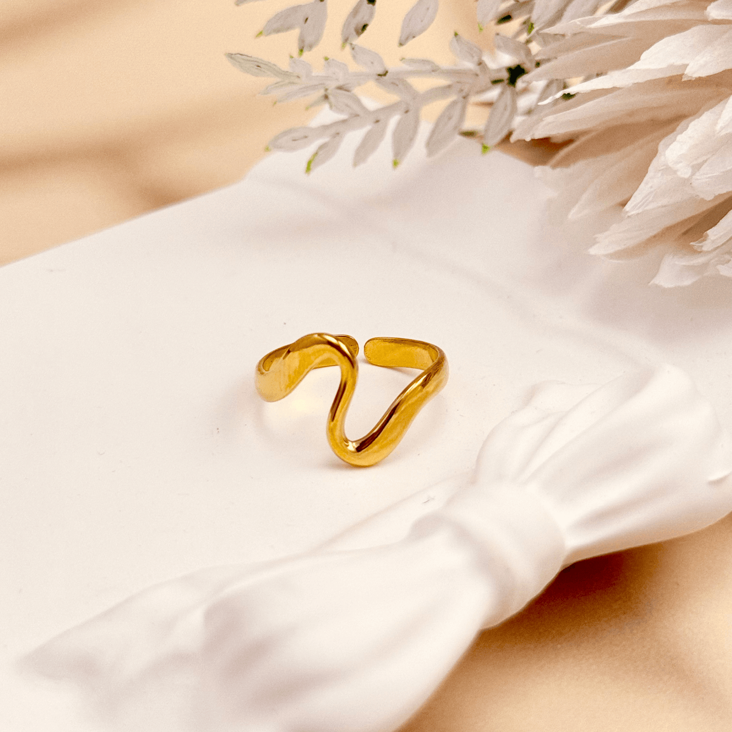 Gold minimalist open ring with soft wave-shaped design on white ceramic background.