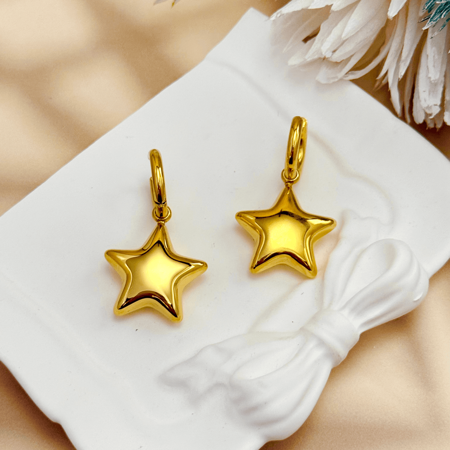 Gold hoop earrings with puffed star charms, made of PVD gold-plated stainless steel, displayed on a white stand.