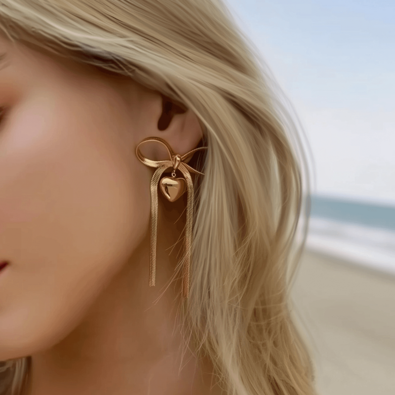 Woman wearing statement gold earrings with a ribbon and heart charm design, perfect for showcasing MXW Jewellery’s elegant earring collection.