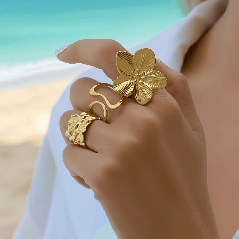 stylish gold rings from MXW Jewellery, including a bold flower design, organic texture band, and modern wave shape, perfect for a summer beach vibe.