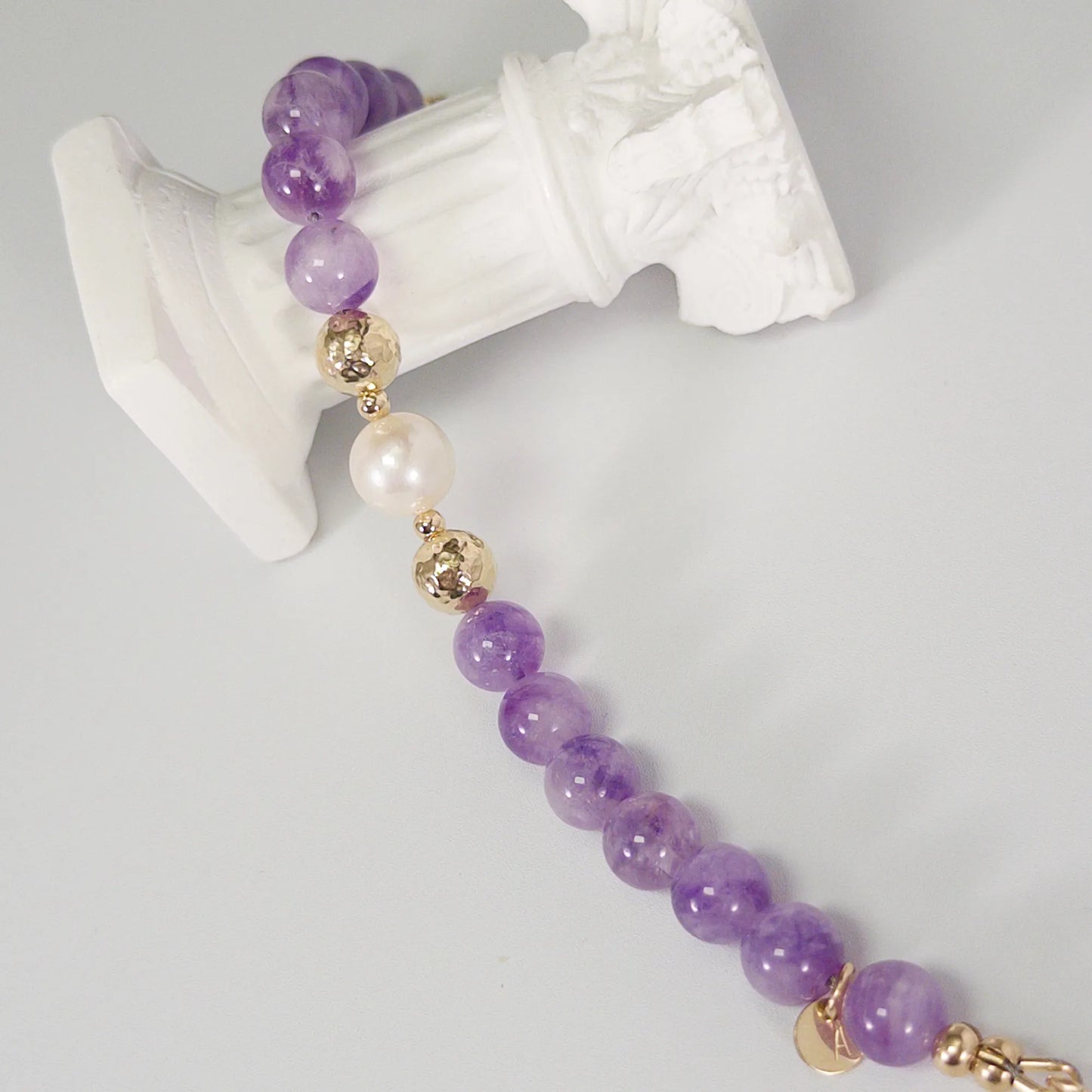 A beaded bracelet featuring Amethyst beads, premium freshwater pearl, and stamped initial disc, 14k gold filled. MXW Jewellery.