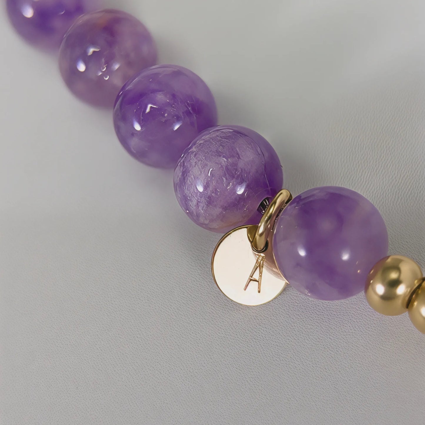 A beaded bracelet featuring Amethyst beads, premium freshwater pearl, and stamped initial disc, 14k gold filled. MXW Jewellery.