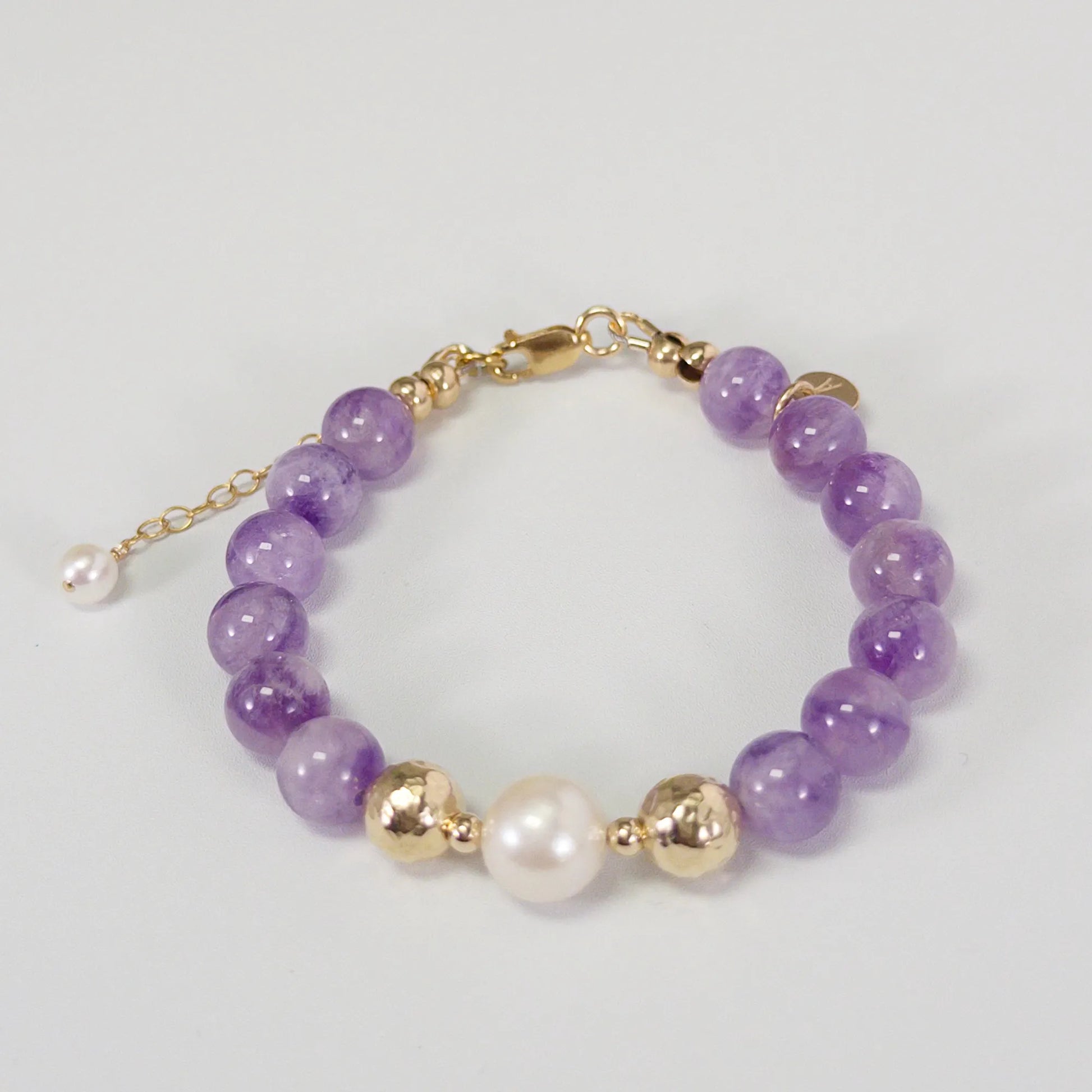 A beaded bracelet featuring Amethyst beads, premium freshwater pearl, and stamped initial disc, 14k gold filled. MXW Jewellery.