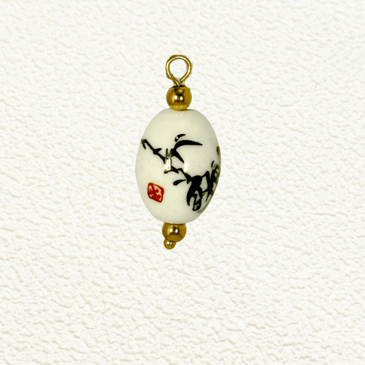 Oval ceramic charm featuring black bamboo brushstroke art and red Chinese seal, accented with gold beads
