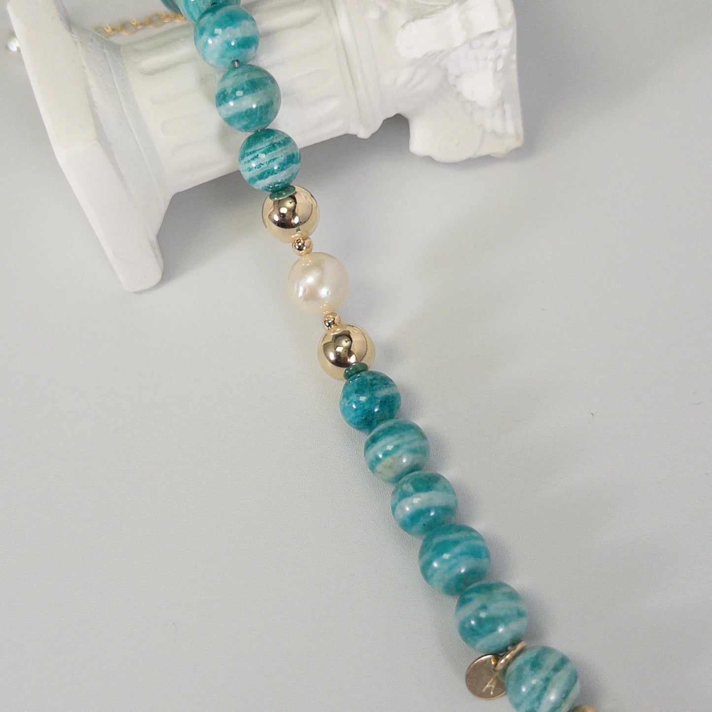 A beaded bracelet featuring banded amazonite gemstone beads, premium freshwater pearl, and personalised stamped initial disc, 14k gold filled. MXW Jewellery